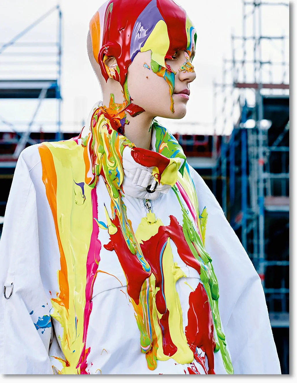 Junge trägt weiße Jacke, die mit bunten Farben verschmiert ist, im Hintergrund eine Baustelle.