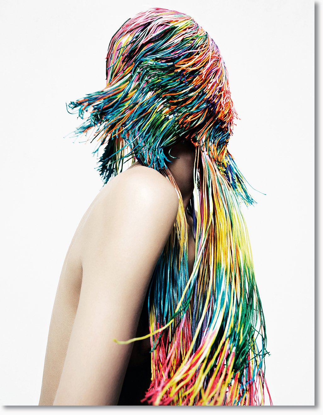 Person mit langen, bunten, gewellten Haaren, die in alle Richtungen fliegen, vor weißem Hintergrund. Kein Gesicht sichtbar.