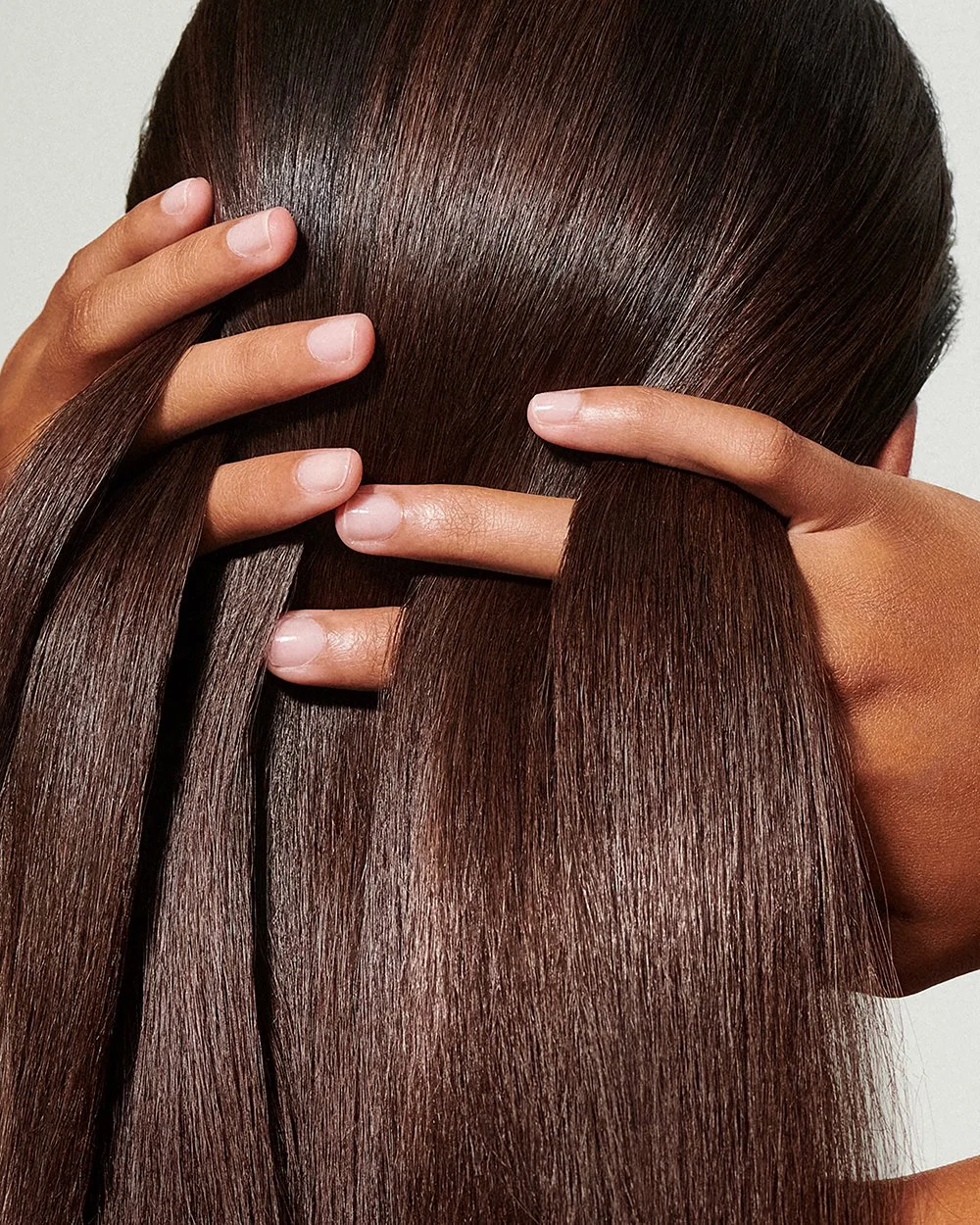 Nahaufnahme von einer Person mit glatten, braunen Haaren, die sie mit beiden Händen berührt.
