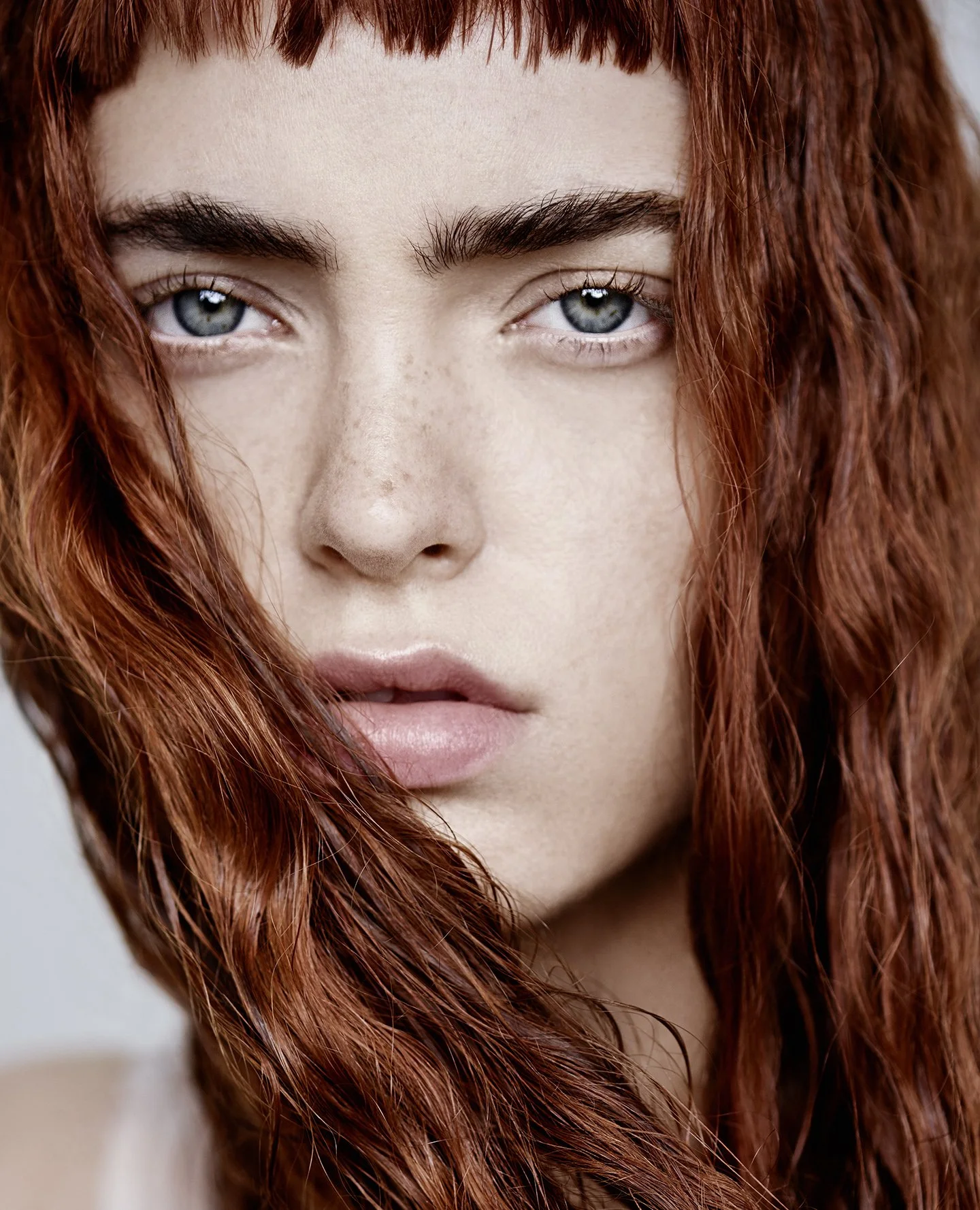 Nahaufnahme eines Mädchens mit roten, lockigen Haaren, blauen Augen und natürlichem Make-up.