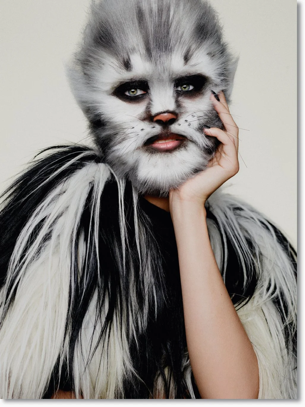 Person mit einem aufwändigen Katzen-Make-up und Kostüm, die die Hand an das Gesicht legt.