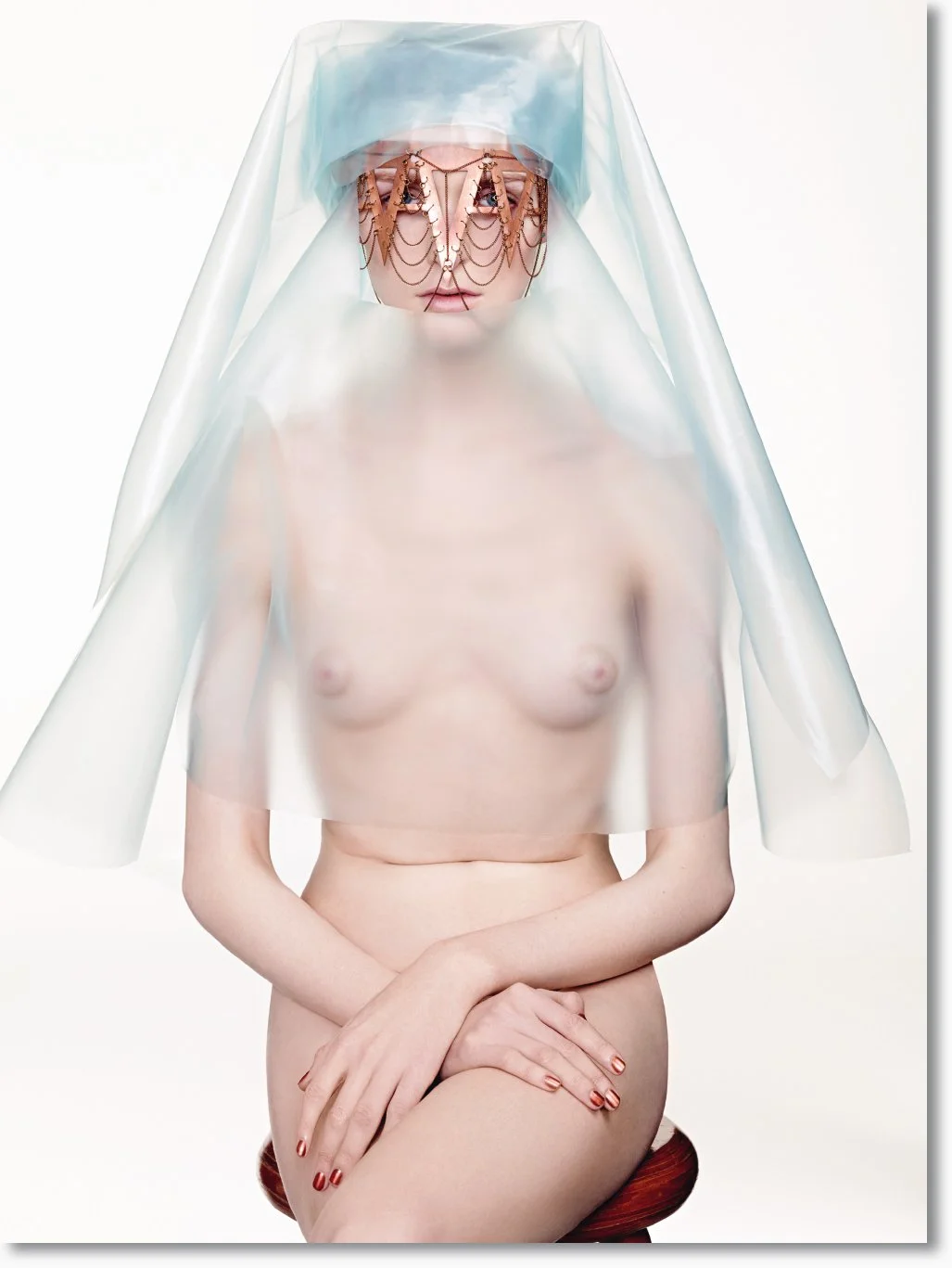 Nackte Frau mit Gesichtsbedeckung und transparentem Schleier, sitzt auf einem Stuhl.