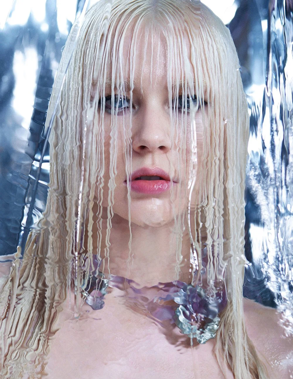 Nahaufnahme eines blonden Mädchens, das hinter einer transparenten, gewellten Kunststofffolie steht, mit Wasser auf der Haut und nassen Haaren.