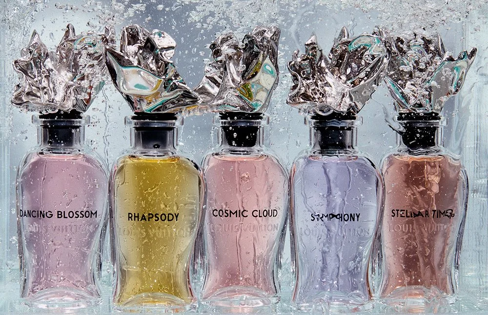 Fünf Parfümflaschen mit unterschiedlich gefüllten Parfümen, jeder mit einem silbernen Deckel und Metallplättchen am Flaschenhals, gefüllt mit farbigen Flüssigkeiten in den Farben rosa, gelb, rosa, lila und rosé.