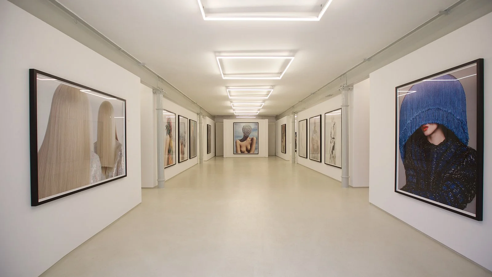 Kunstgalerie mit weißen Wänden und gerahmten Fotos oder Gemälden, beleuchtete Decke, leeres helle Parkettboden.