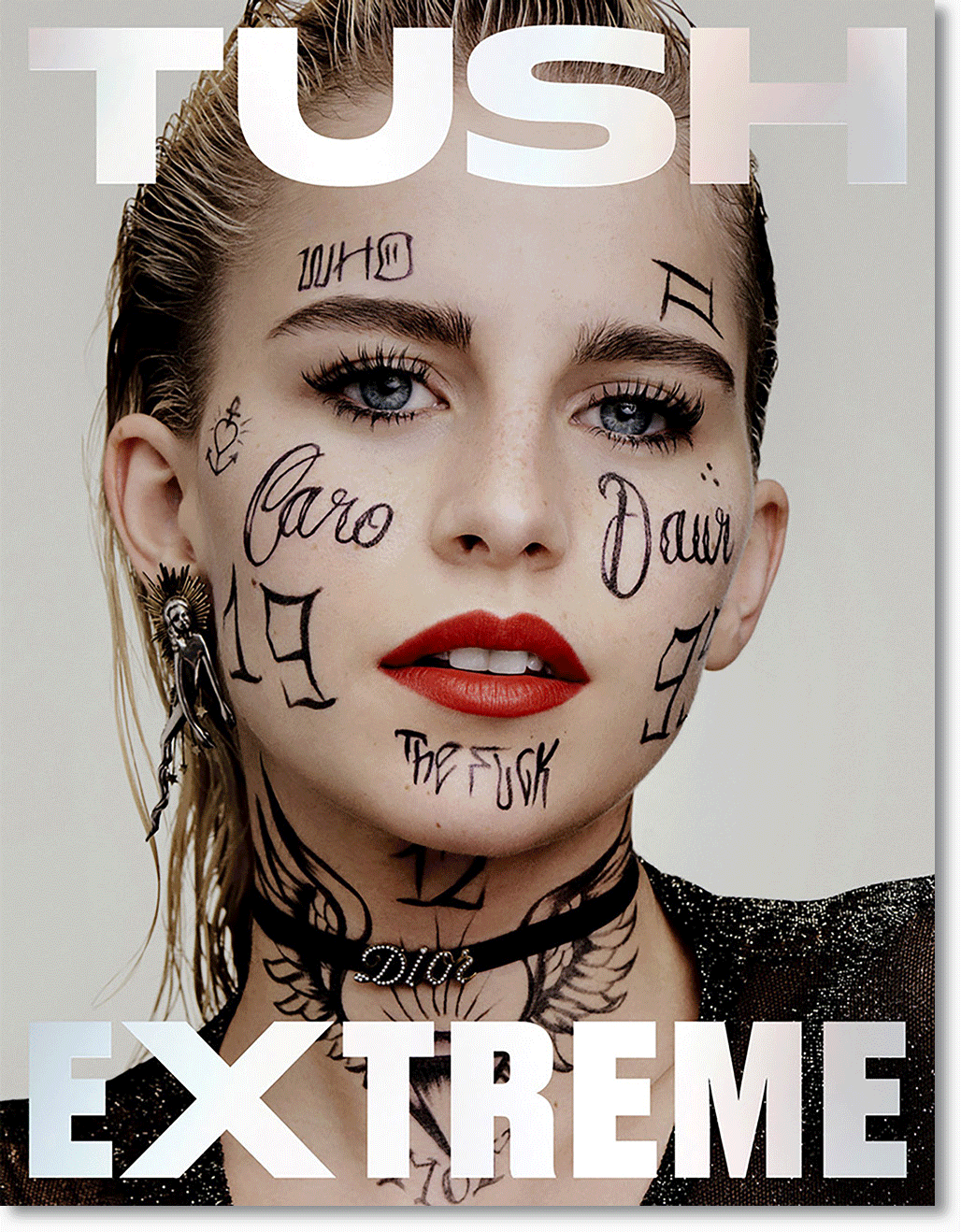 Nahaufnahme eines Models mit Tattoos auf Gesicht, Hals und Ohr, rote Lippen, Blondhaar und blauen Augen, die auf einem Glamour-Fachmagazin mit dem Titel "TUSH EXTREME" abgebildet ist.