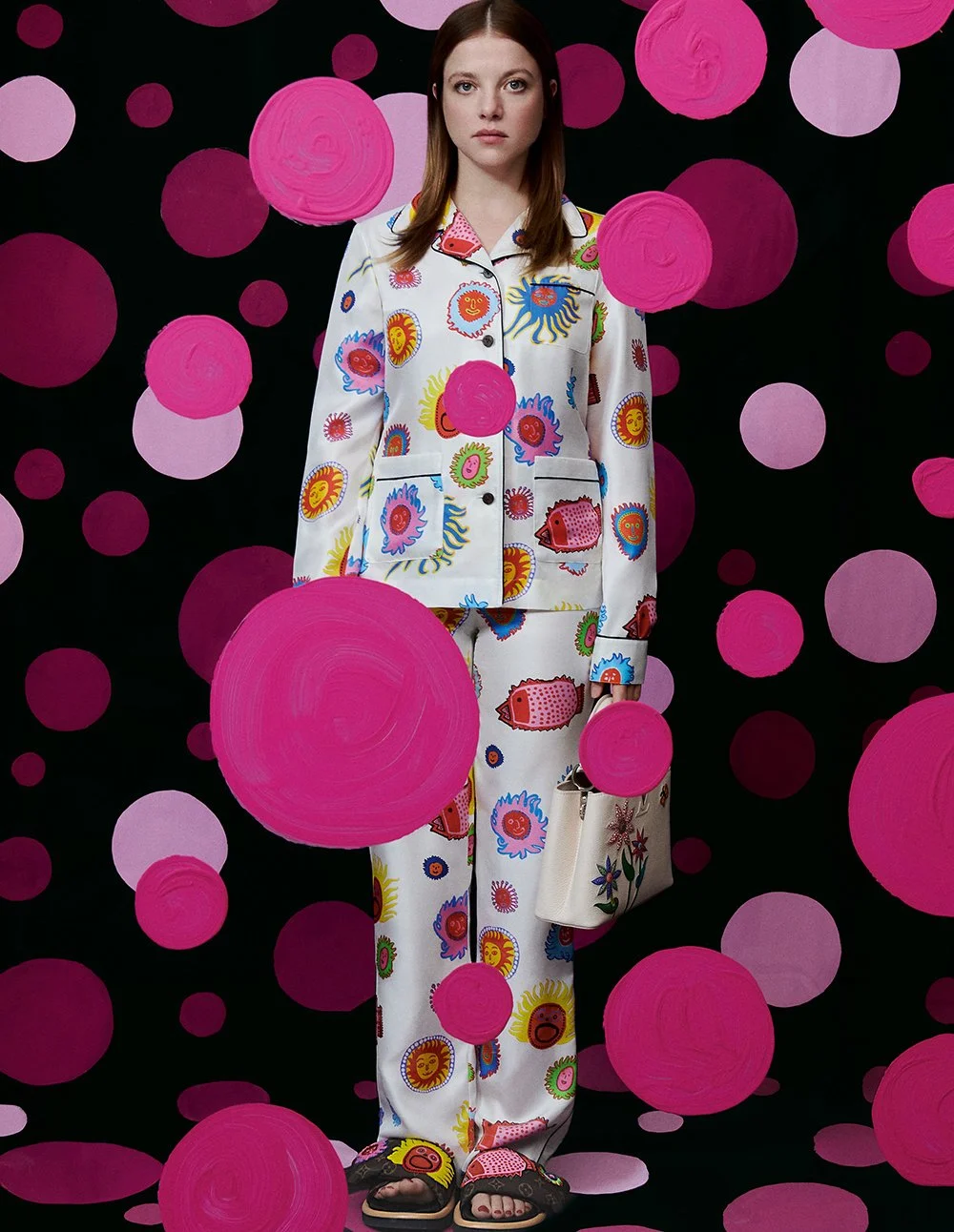 Frau in Pyjama mit buntem, sonnigem Druck steht vor einem schwarz-pinken Volumenhintergrund mit großen pinken Kreisen.