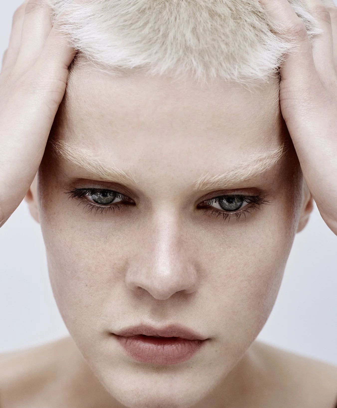 Nahaufnahme eines Menschen mit blonder, kurz geschnittener Frisur, der die Hände an den Kopf legt.