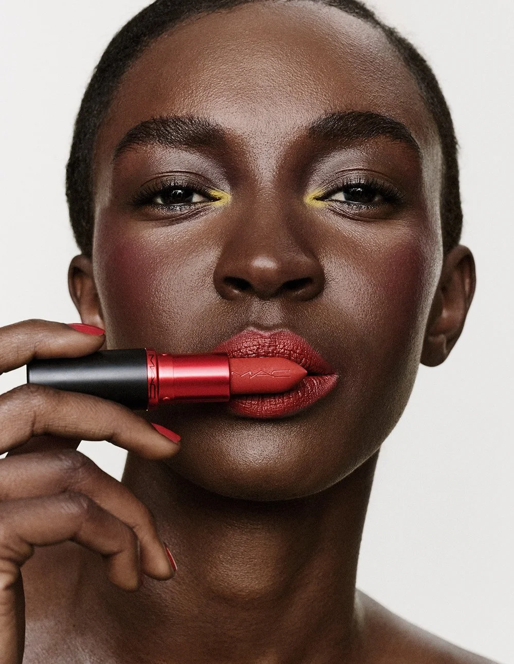 Nahaufnahme eines schwarzen Mädchens mit dunkler Haut, das roten Lippenstift trägt, den Lippenstift an den Lippen hält und in die Kamera schaut.