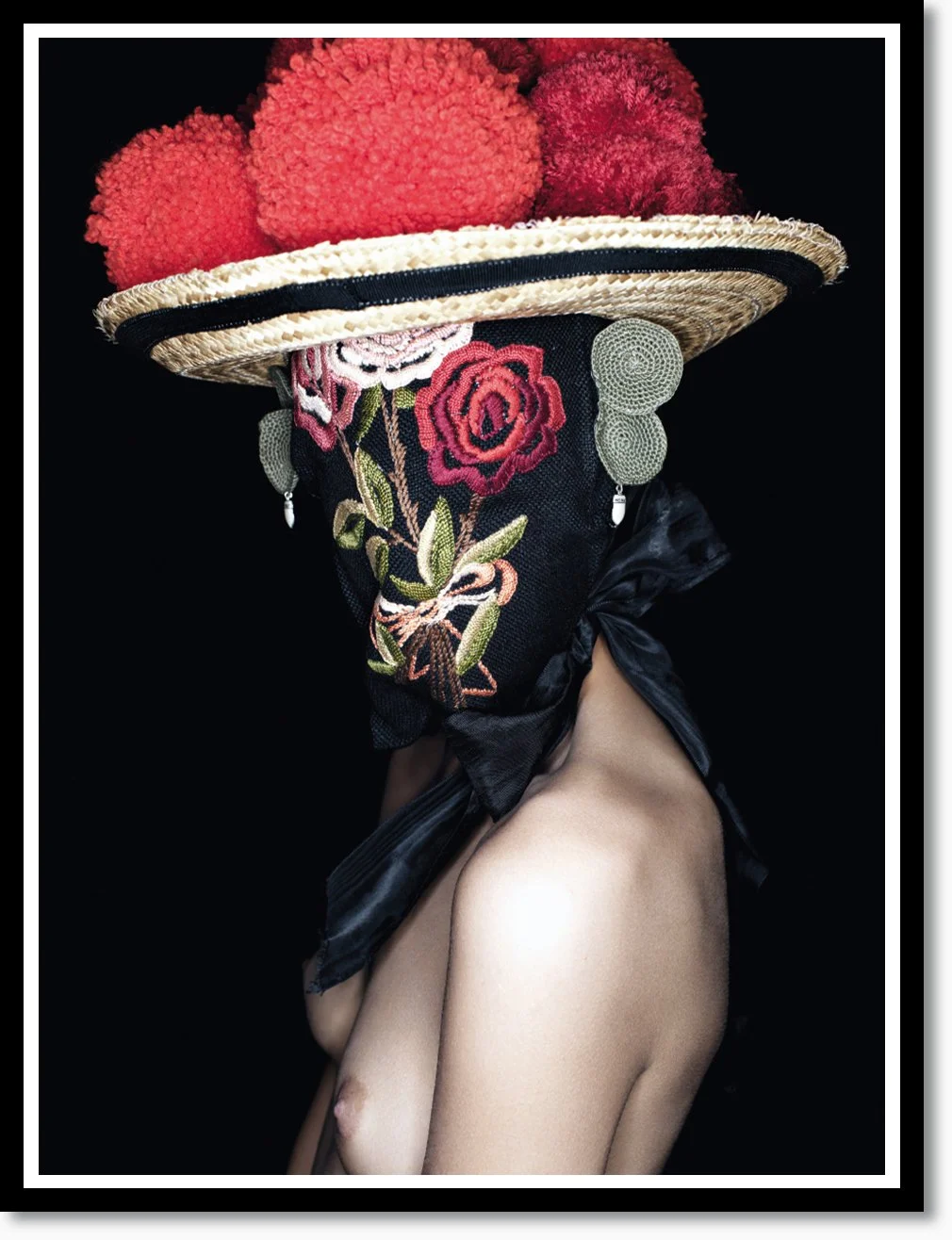 Kunstvolle Darstellung einer Person mit einem großen, breitkrempigen Strohhut, verziert mit roten Pompons. Das Gesicht ist durch einen schwarz-bestickten Schal bedeckt, der mit floralem Muster und grünen Applikationen geschmückt ist. Die Person ist h