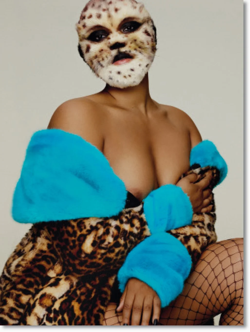 Person mit Leoparden-Maske, in einem blauen und Leoparden-Mantel, sitzend, mit Fischernetz-Strümpfen.