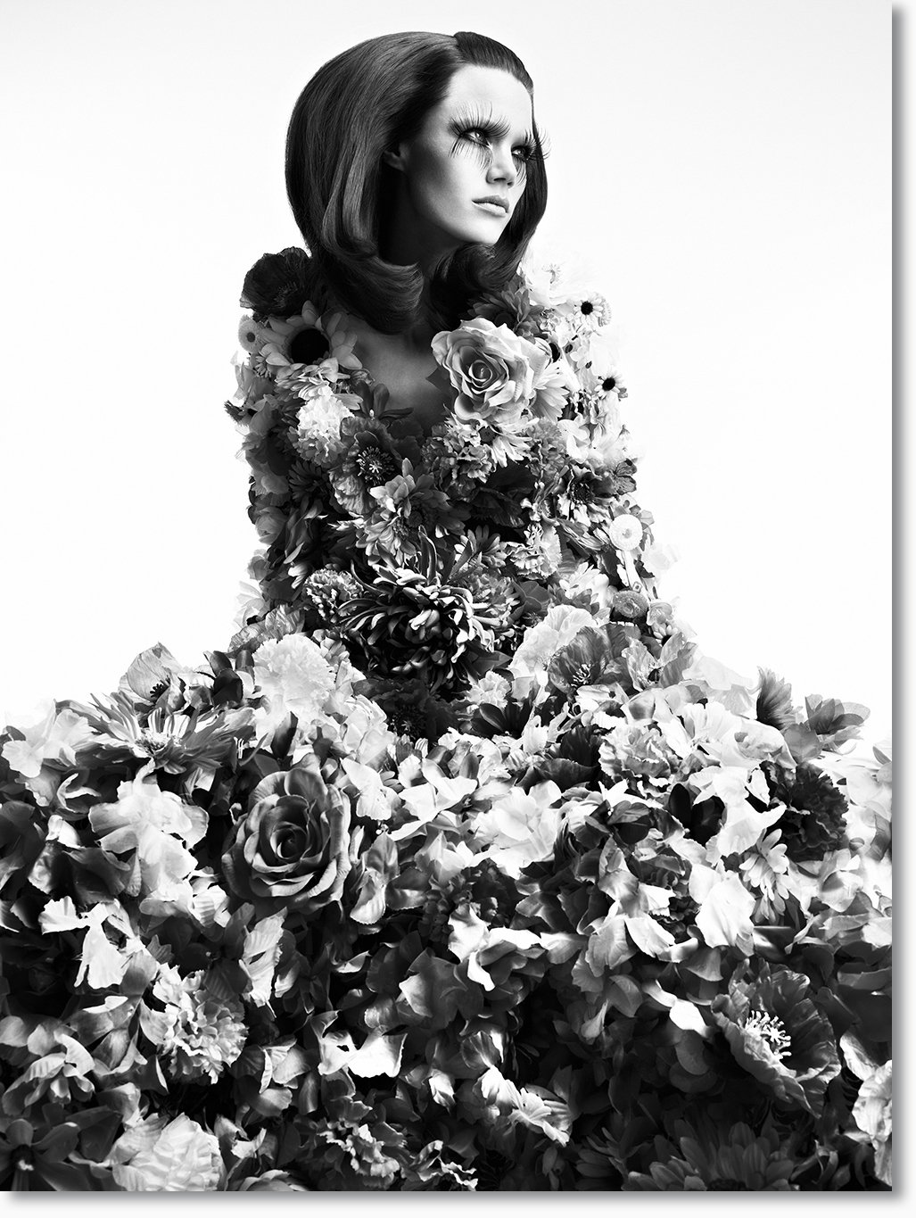 Schwarz-Weiß-Fotografie einer Frau, die mit einer Vielzahl von Blumen bedeckt ist, mit dramatischem Make-up und vollem roten Haar.