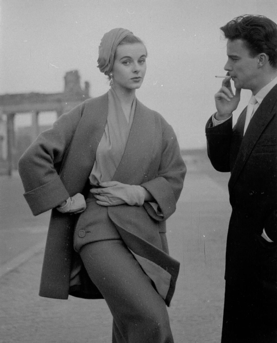Schwarz-weiß-Foto eines Mannes und einer Frau, die auf einer Bühne stehen, die Frau schaut direkt in die Kamera, während der Mann raucht.