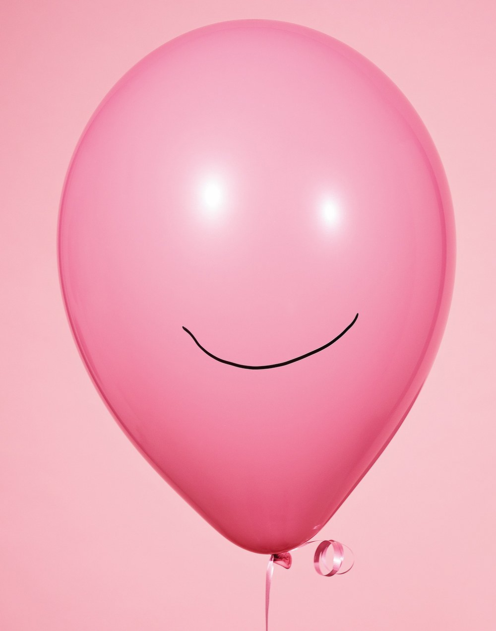 Ein pinker Luftballon mit einem lachenden Gesicht, auf hellem pinkem Hintergrund.