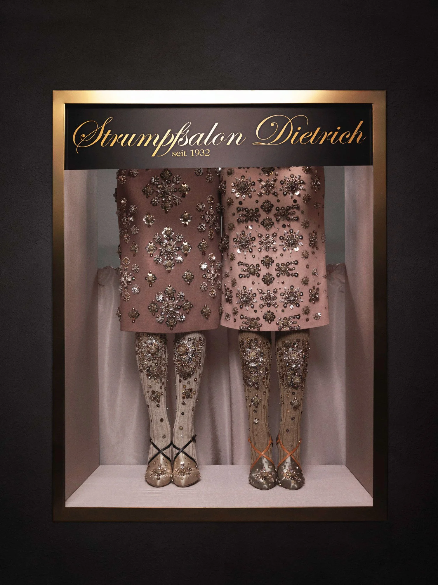 Display of two vintage embroidered dress mannequins, showcasing detailed floral beading and embellishments, with the sign 'Strumpfsalon Dietrich seit 1932' above.