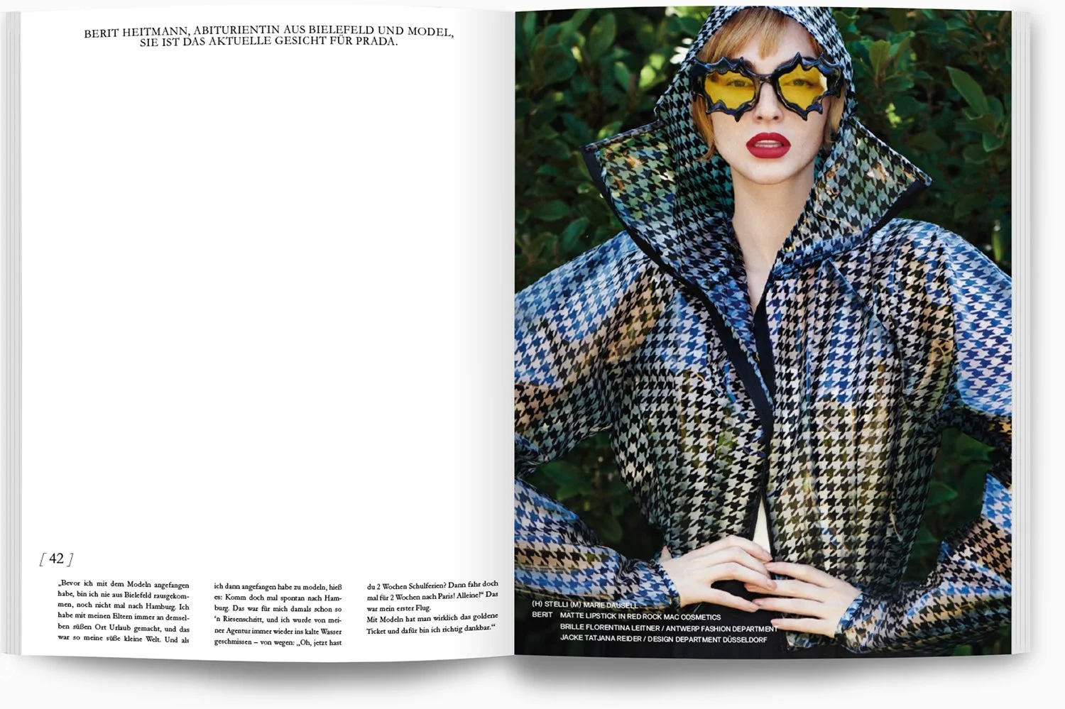 Model trägt Hahnentritt-Mantel und ausgefallene Sonnenbrille, steht vor grünen Blättern in einem Außenbereich.