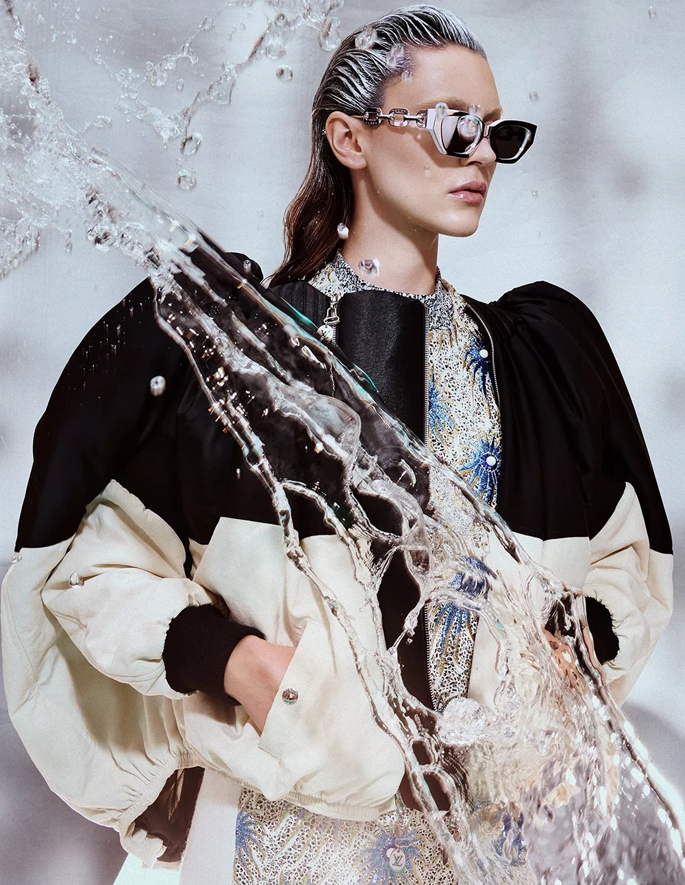 Frau mit großen Sonnenbrillen, waschendem Haar, Schwarz-weißer Jacke, teilweise mit wasserspritzendem Wasser