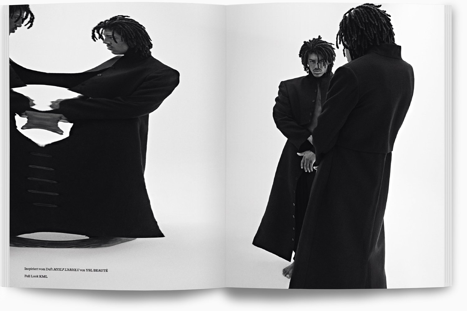 Zwei Männer in schwarzen Mänteln stehen vor einem weißen Hintergrund, eine der Männer blickt ernsthaft, während die andere Person den Rücken zur Kamera hat.