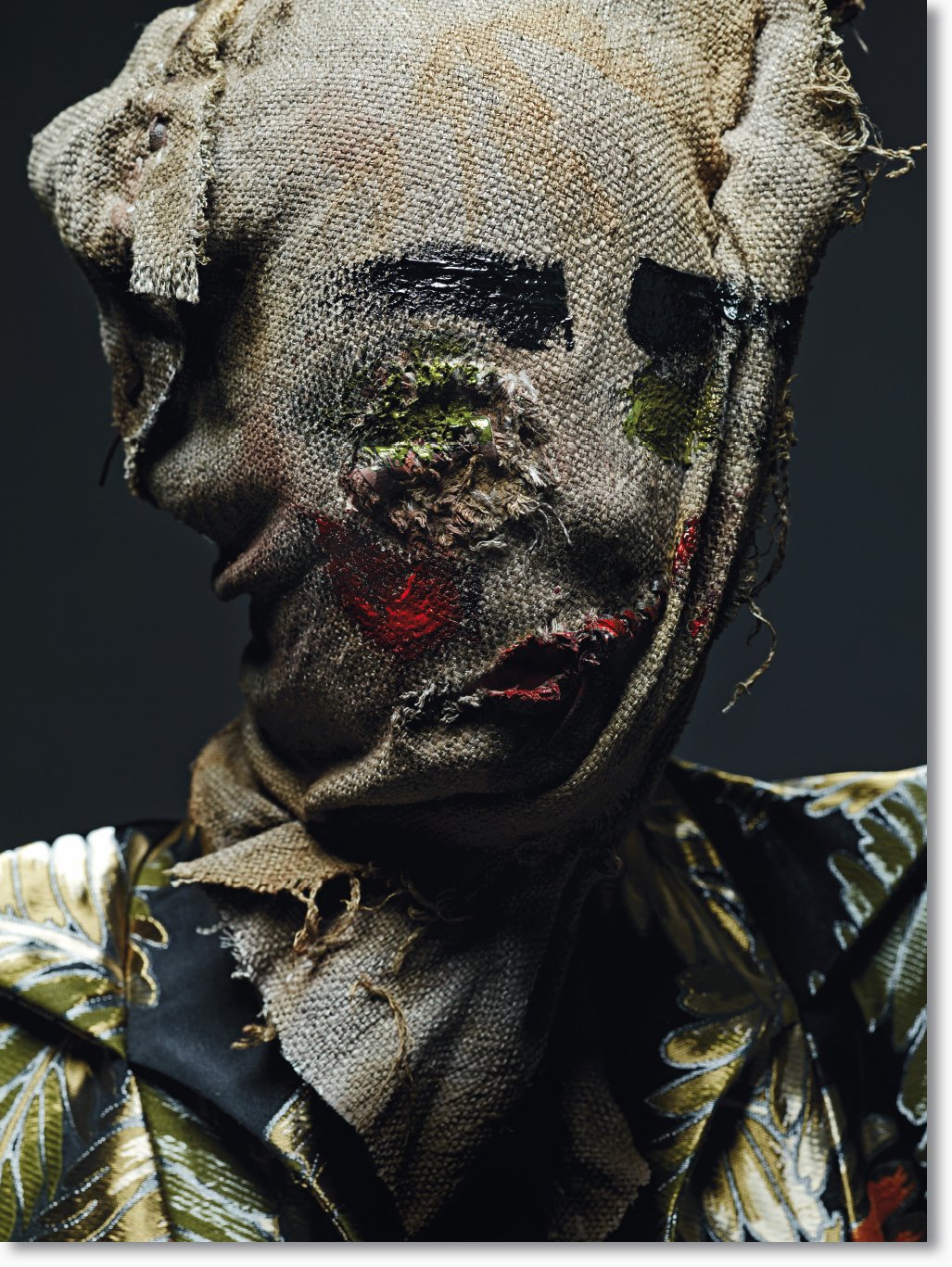 Kunstwerk eines Mischmasch-porträts mit einem zerrissenen Stoffgesicht, hebt die Augenbrauen, die Nase und den Mund hervor, trägt ein blumenmusterndes Hemd, dunkler Hintergrund.