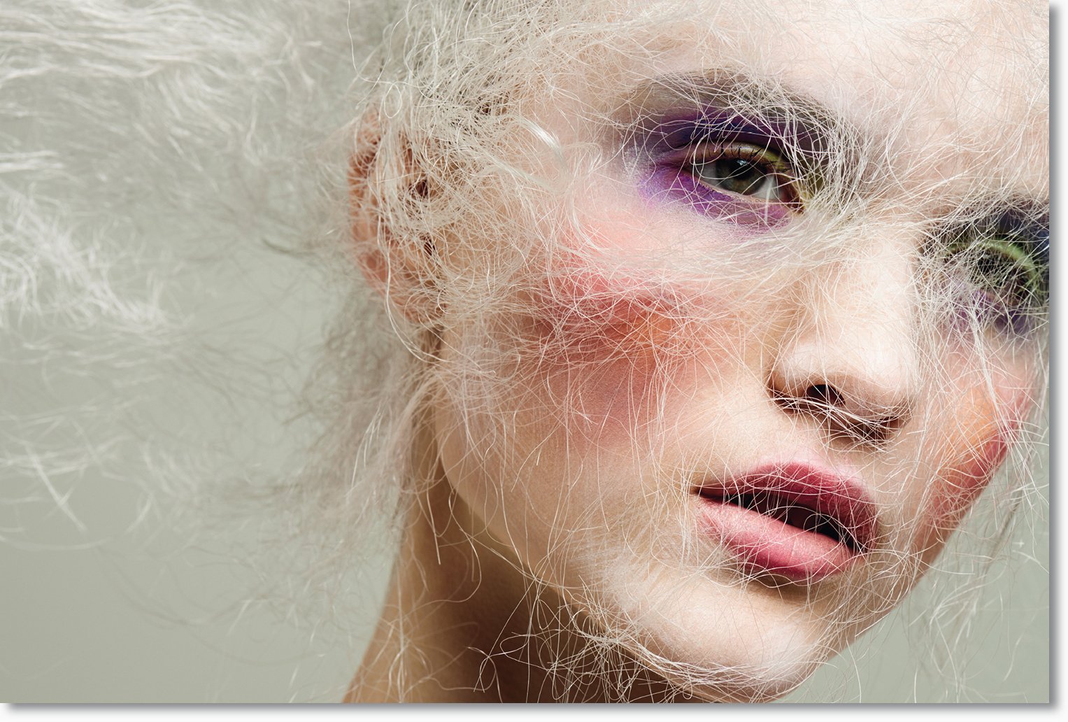 Nahaufnahme eines Gesichtsausdrucks mit weißen, lockigen Haaren, mit buntem Make-up um die Augen und auf den Lippen.