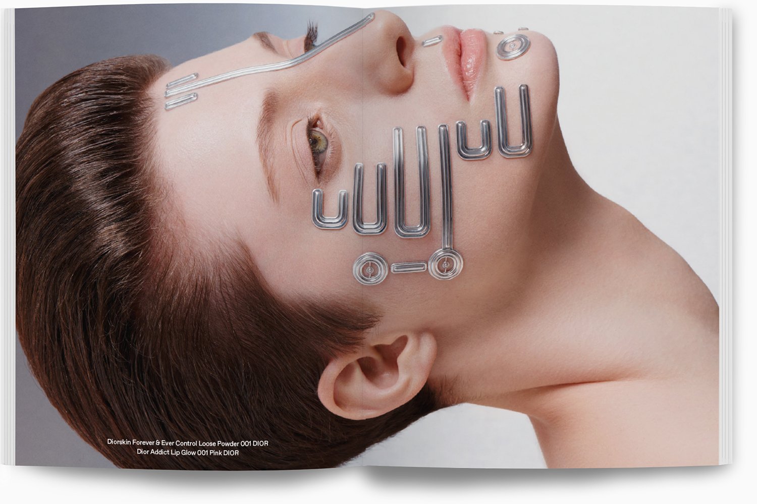 Nahaufnahme eines Frauenkopfes mit glattem, braunem Haar liegt seitlich. Es werden Make-up-Produkte wie Lipgloss und Konturenstifte gezeigt, mit metallischen Wörtern, die auf den Bildern liegen.