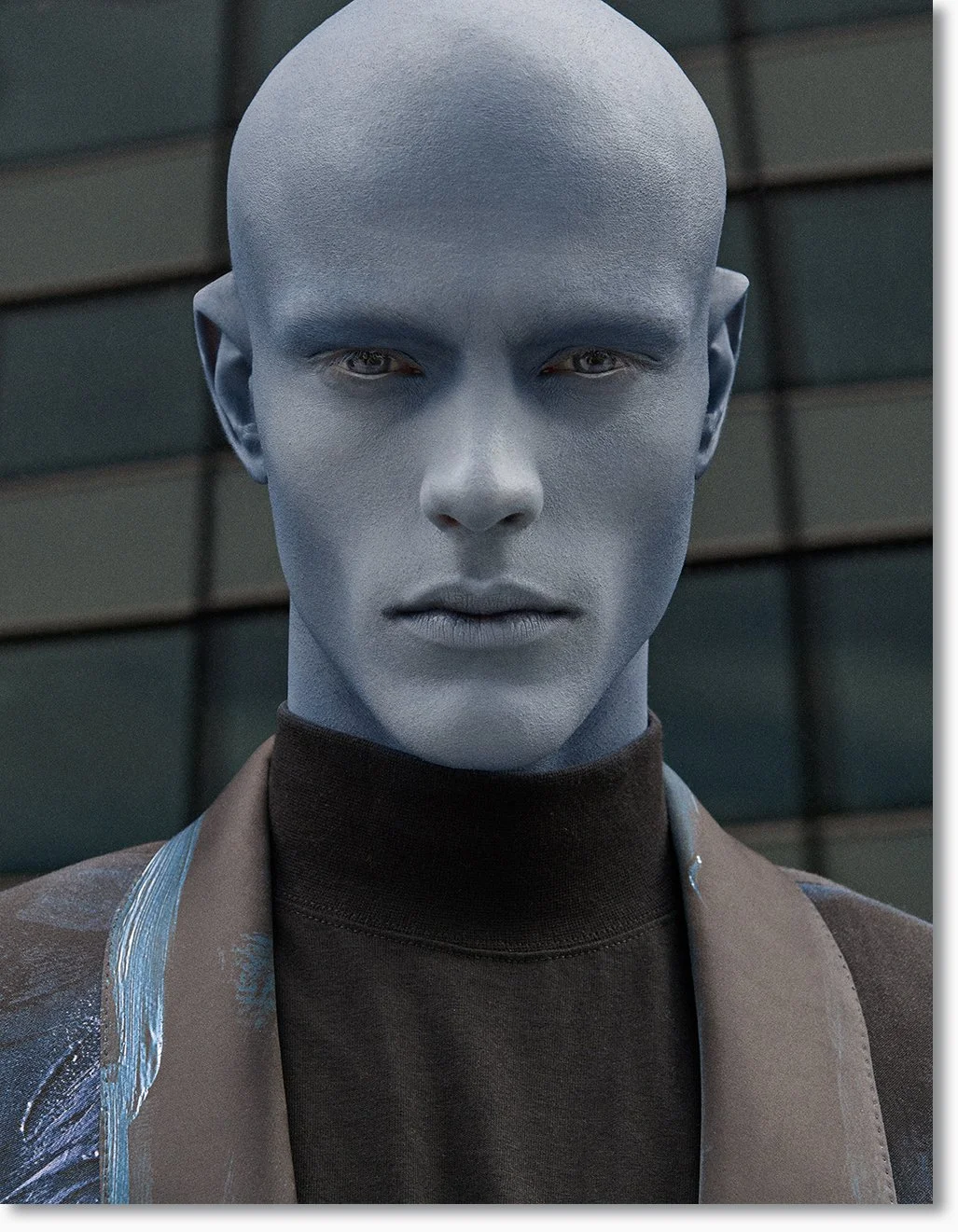 Nahaufnahme eines humanoiden Wesens mit blauer Haut, glattem Kopf, blauen Augen und neutralem Gesichtsausdruck, vor einem modernen Gebäude.