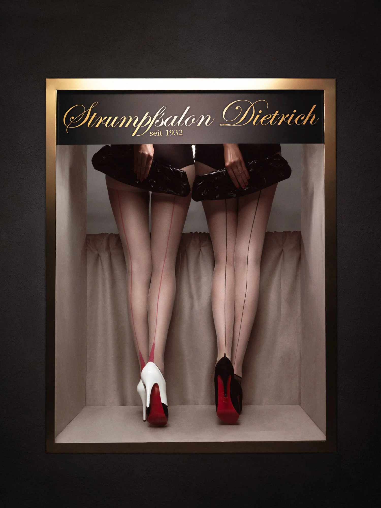 Display case with two pairs of legs wearing high heels and sheer stockings, under a sign that reads "Strumpfsalon Dietrich seit 1932".