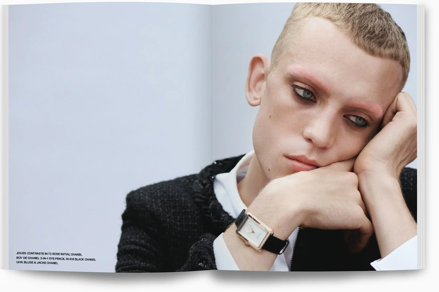 Eine Frau mit kurzen blondem Haar, die nachdenklich aussieht, trägt eine schwarze Jacke und ein weißes Hemd. Sie trägt eine Armbanduhr. Sie sitzt mit der rechten Wange auf ihrer rechten Hand.