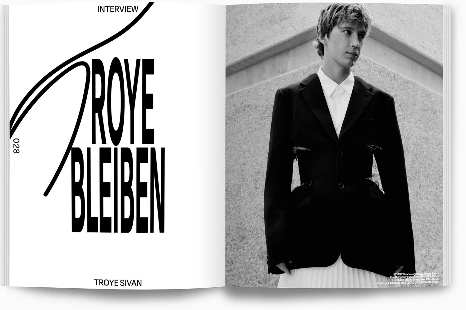 Schwarz-weiß-Fotografie eines jungen Mannes in einem schwarzen Anzug mit weißen Hemd, der neben einer Wand steht. Auf der linken Seite Text im Stil eines Buchs oder Magazins, der lautet: 'Ich möchte bleiben' und darunter 'TROYE SIVAN'.