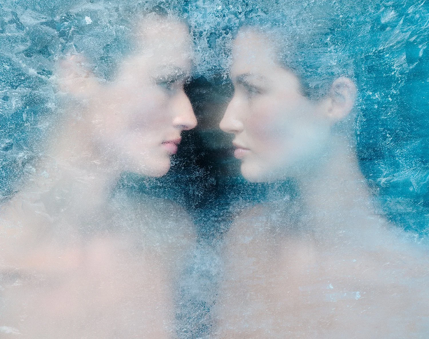 Zwei Frauen stehen sich mit gespiegeltem Gesicht gegenüber, umgeben von Wasser und Eis, wobei sie fast die gleiche Haltung und Mimik zeigen.