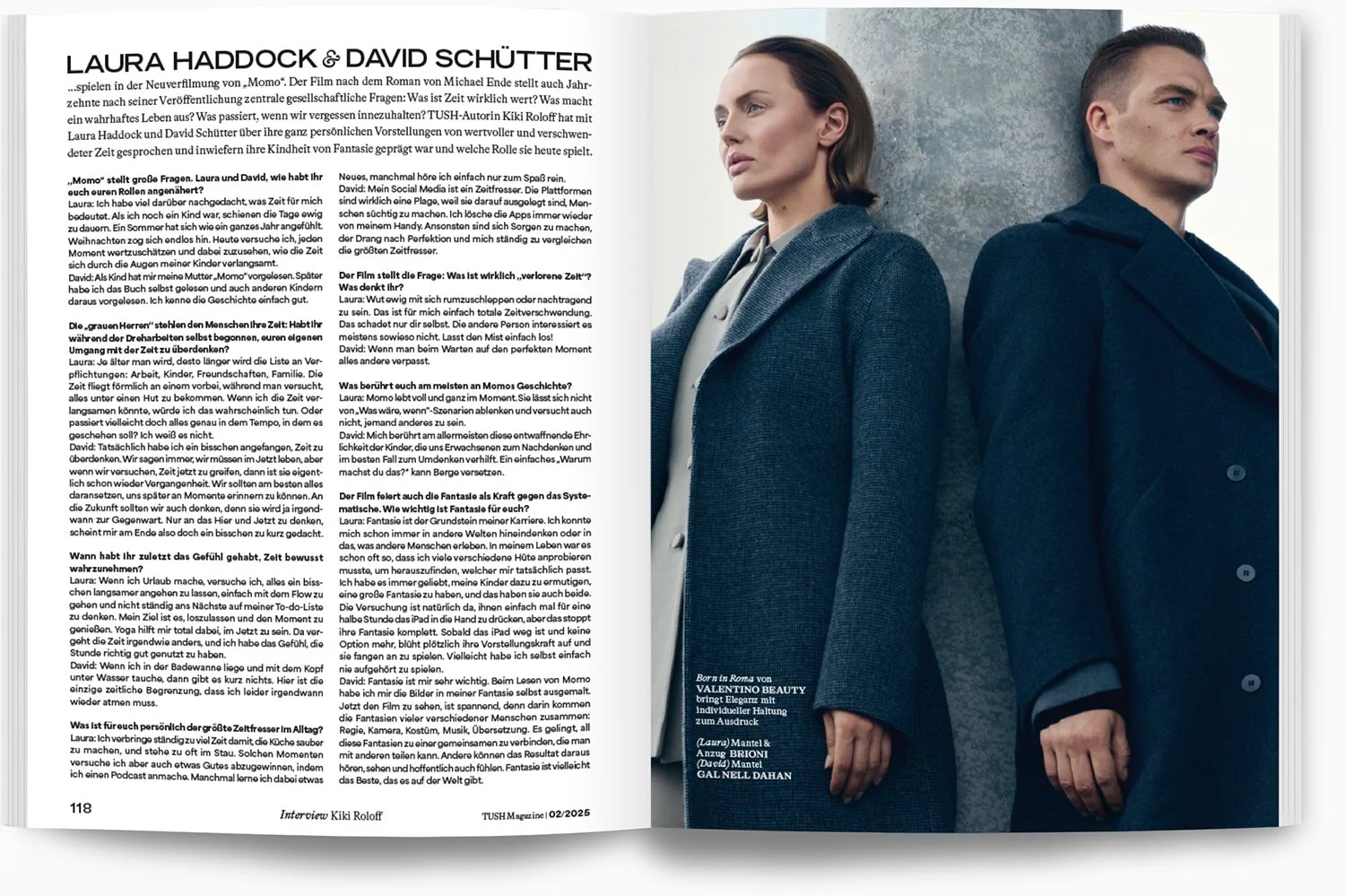 Zwei Menschen stehen nebeneinander vor einer weißen Wand. Die Frau trägt einen grauen Mantel und hat braune, schulterlange Haare. Der Mann trägt eine dunkle Jacke und hat kurze dunkle Haare.