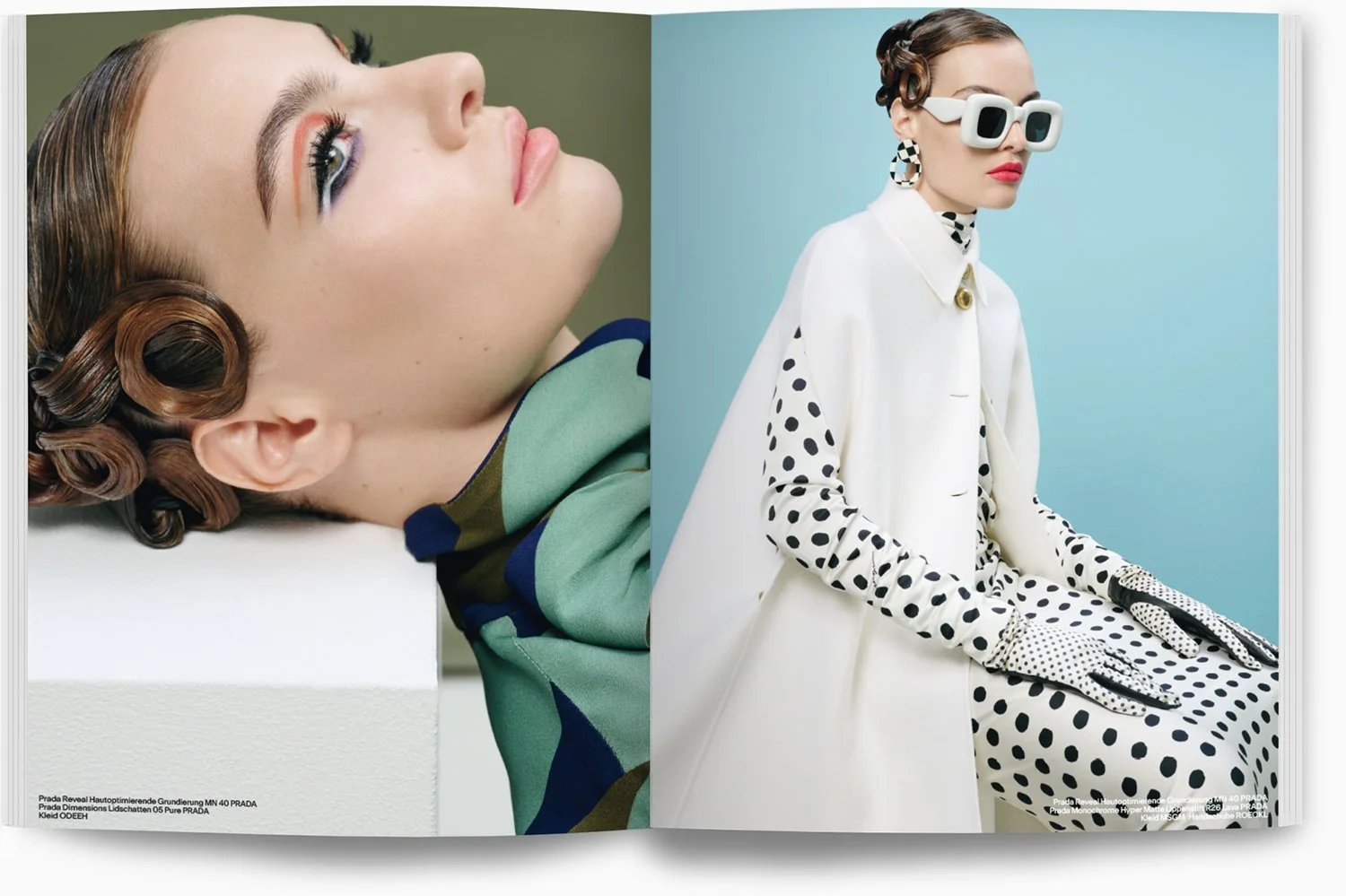 Zwei Frauen, eine liegt auf dem Rücken mit verbundenen, lockigen Haaren und dramatischem Make-up, die andere sitzt in einem weißen Outfit mit schwarz-weiß gepunktetem Muster, trägt große Sonnenbrille, Ohrringe und Handschuhe, vor einem hellblauen Hin