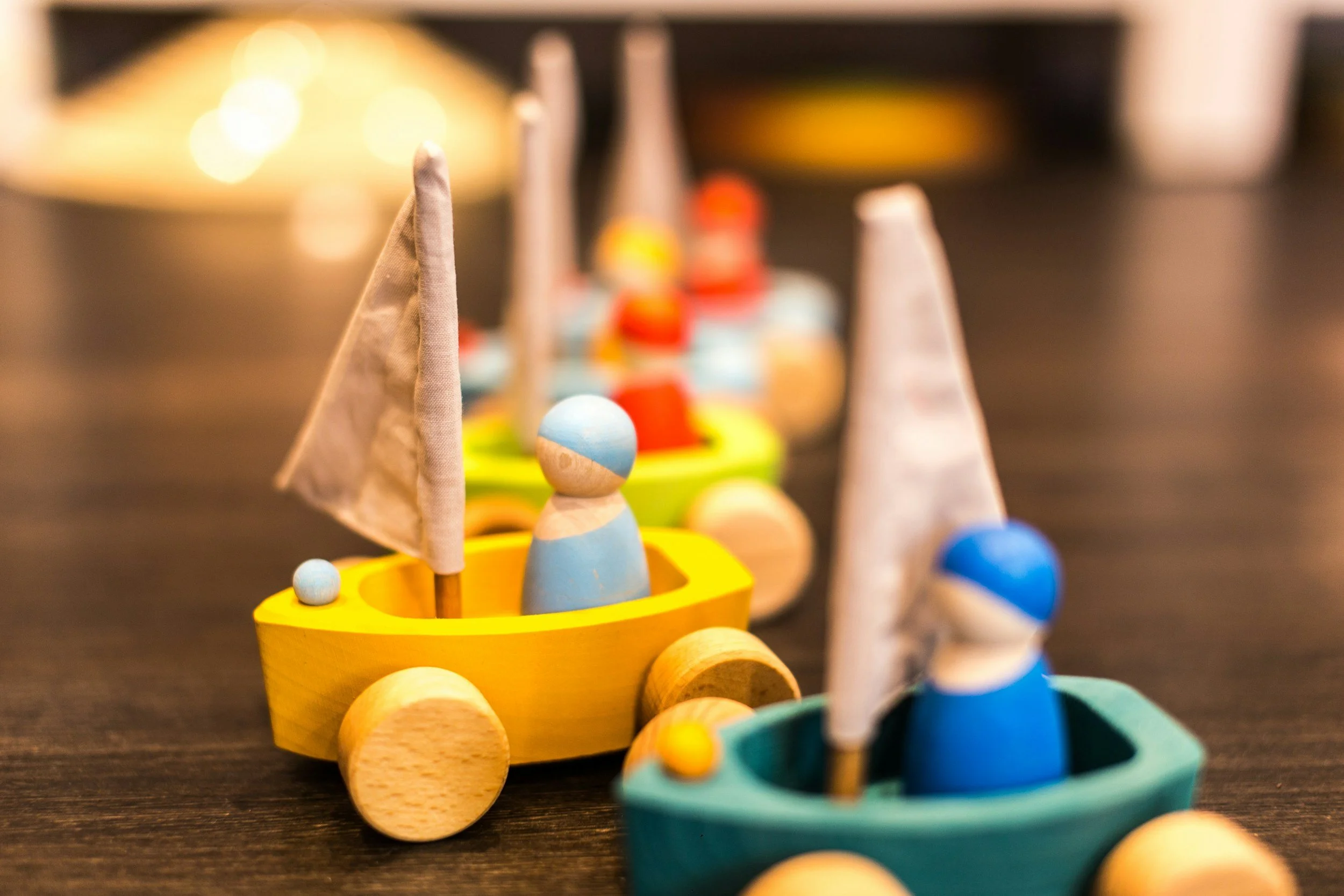 Colorful wooden toy sailboats with painted wooden figures and small balls on a dark surface.