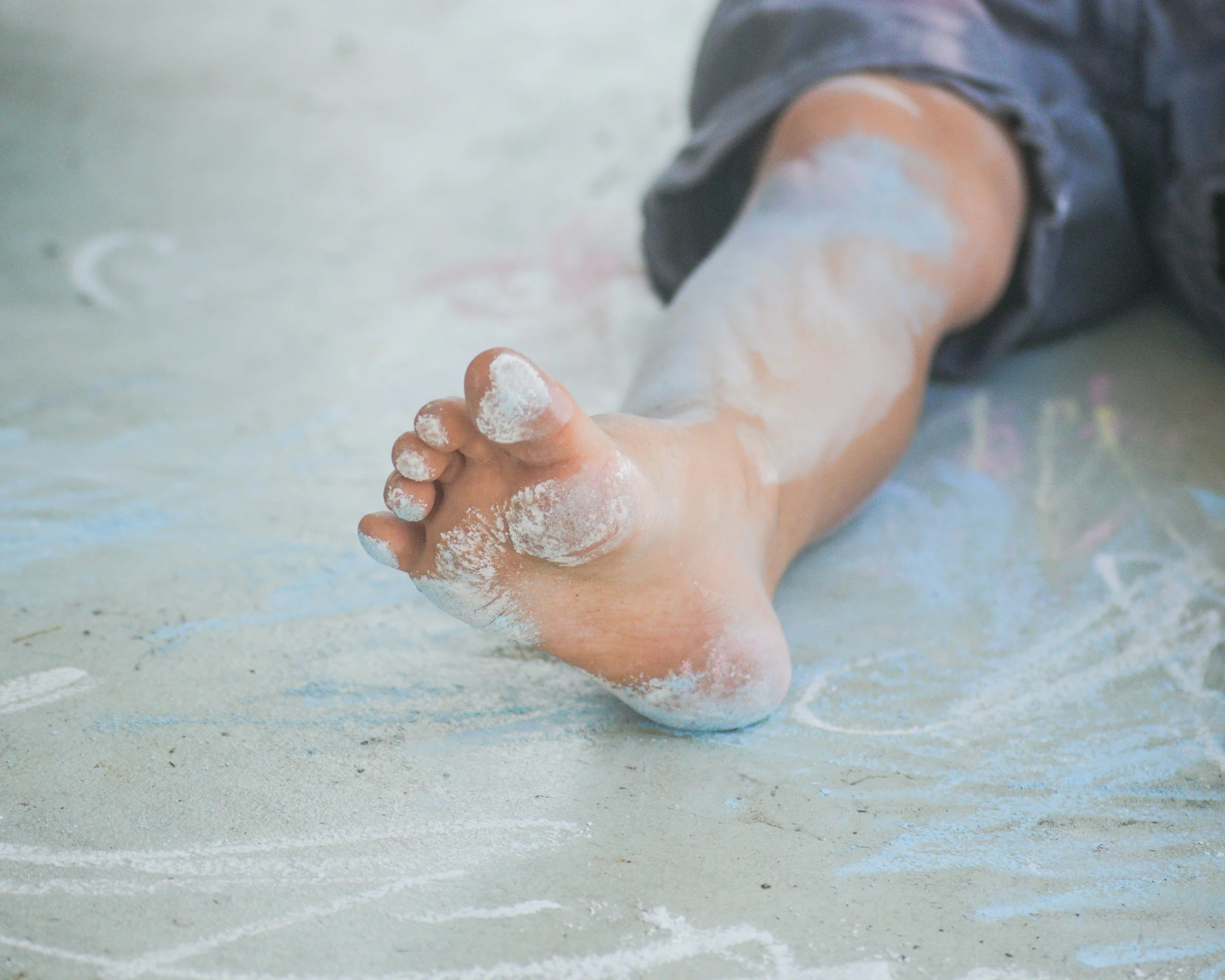 Child's foot covered in white chalk dust, lying on a chalk-covered surface.