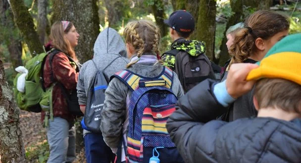 Group of children with backpacks in a forested area.