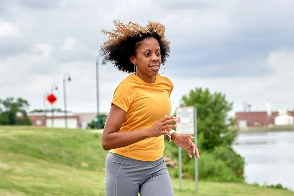A woman in a yellow top runs, curls flying in the wind, on a pedestrian path