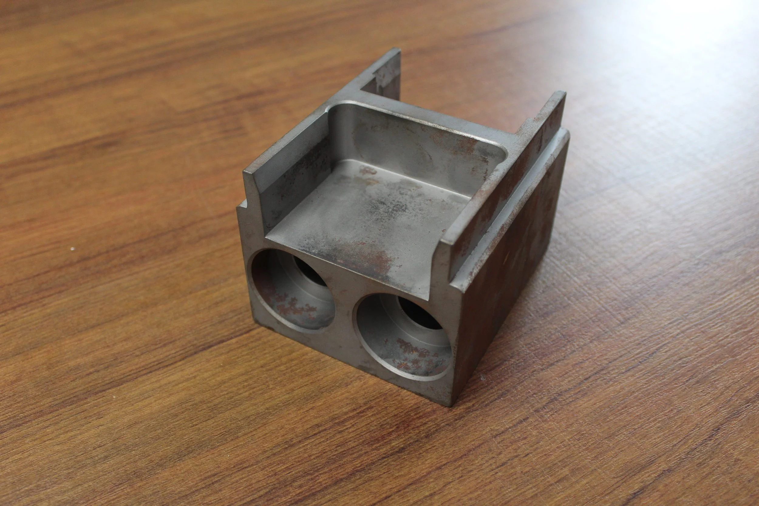 A metal engine block with two circular cylinders, placed on a wooden surface.