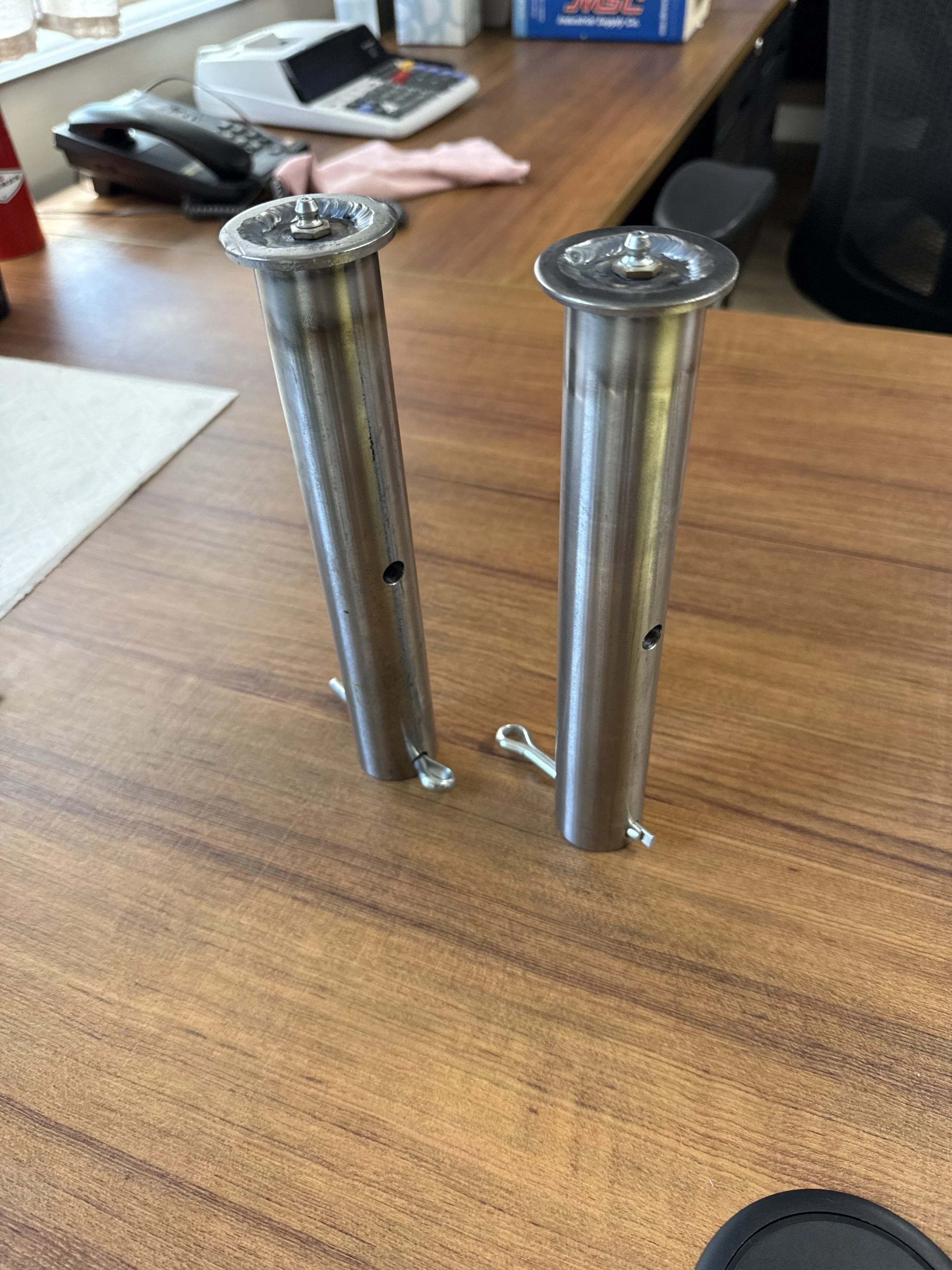 Two metal motorcycle shock absorbers standing upright on a wood desk.