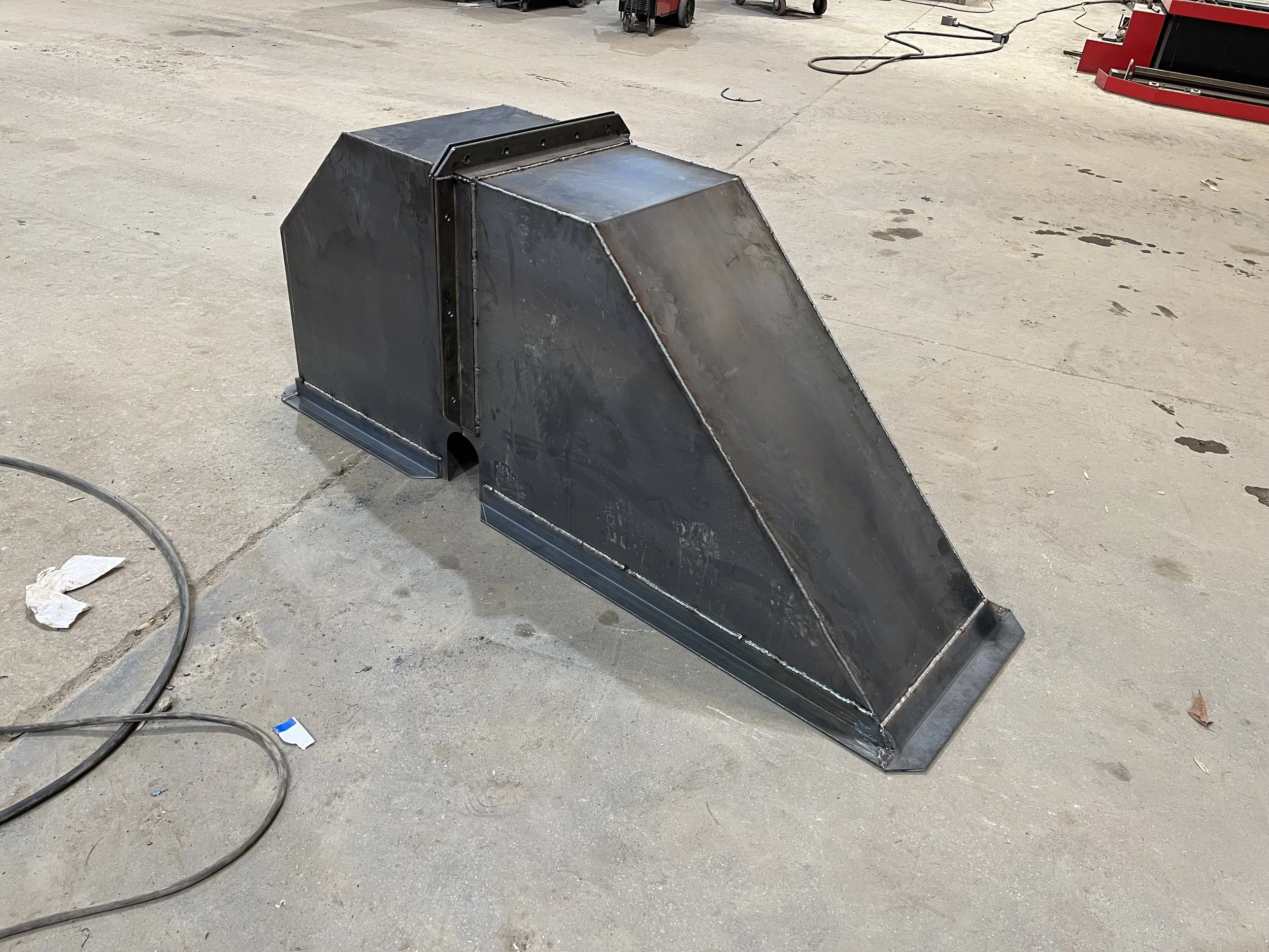 A welded metal duct transition piece in a workshop setting.