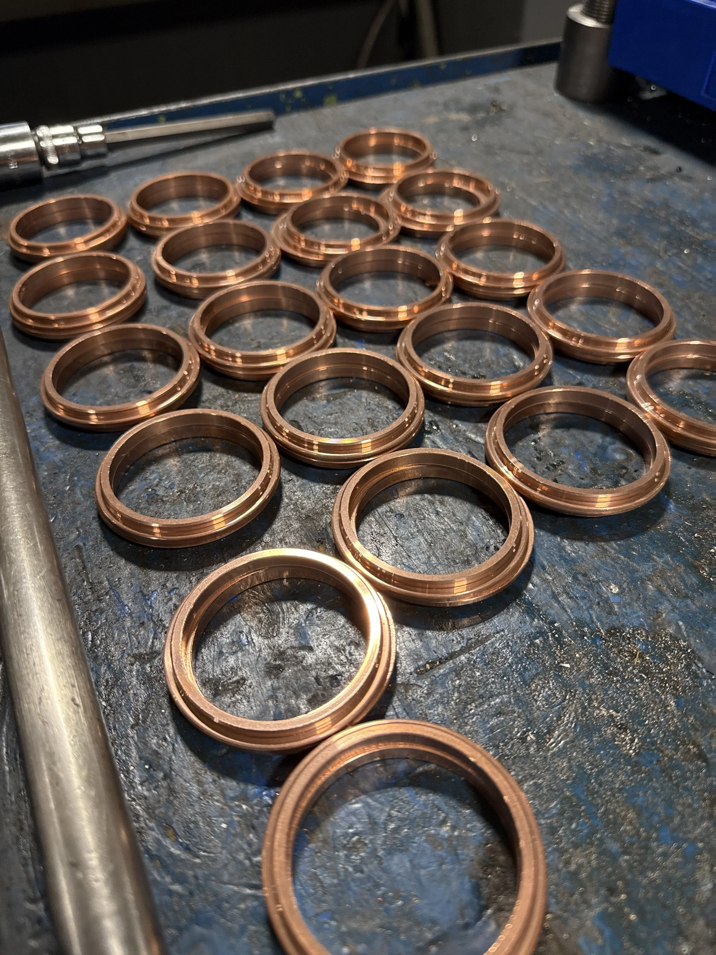 Multiple copper rings arranged on a workbench, with some tools visible nearby.