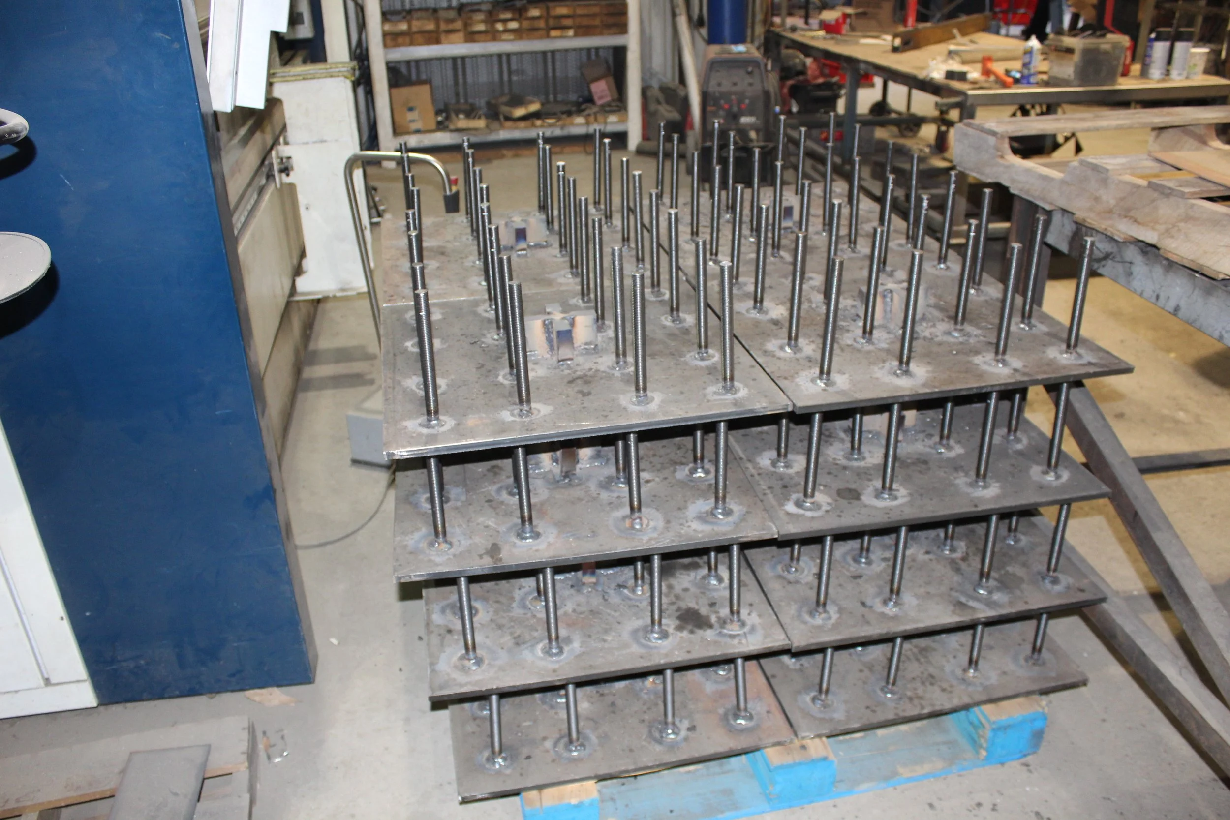 Metal rods welded onto multiple metal plates in an industrial workshop.