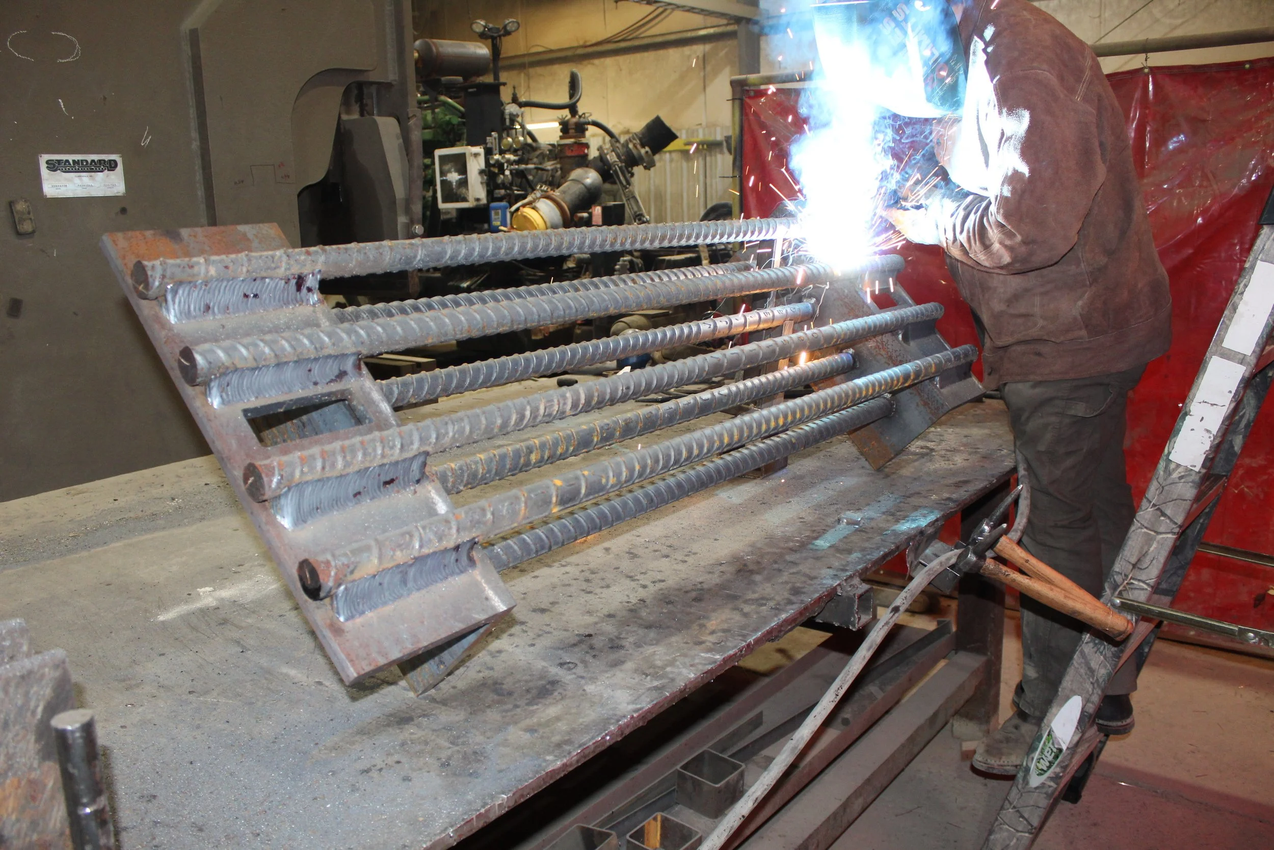 A worker welding reinforced steel bars for construction in an industrial workshop.