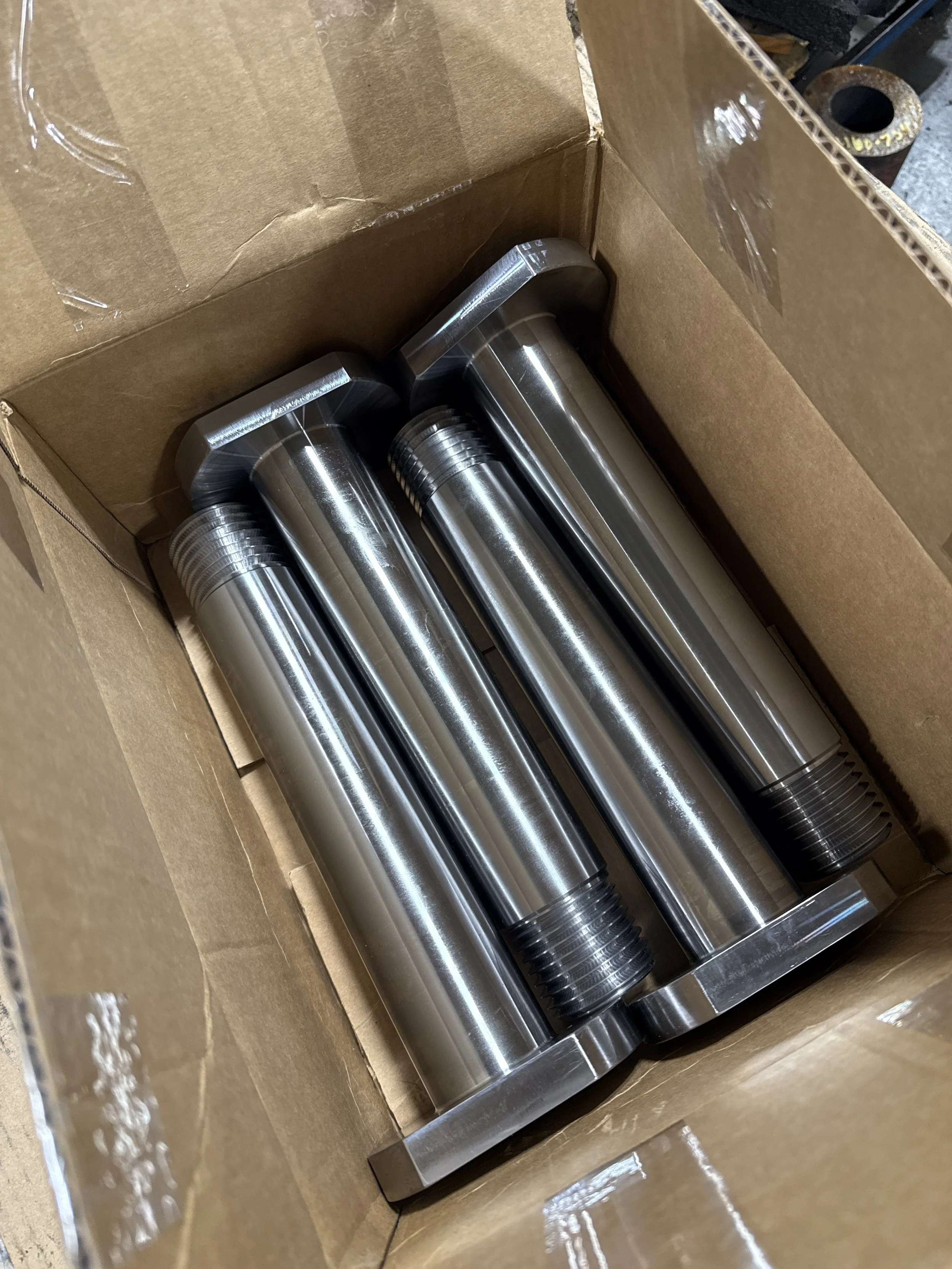 Four metal cylindrical shafts inside a cardboard box.