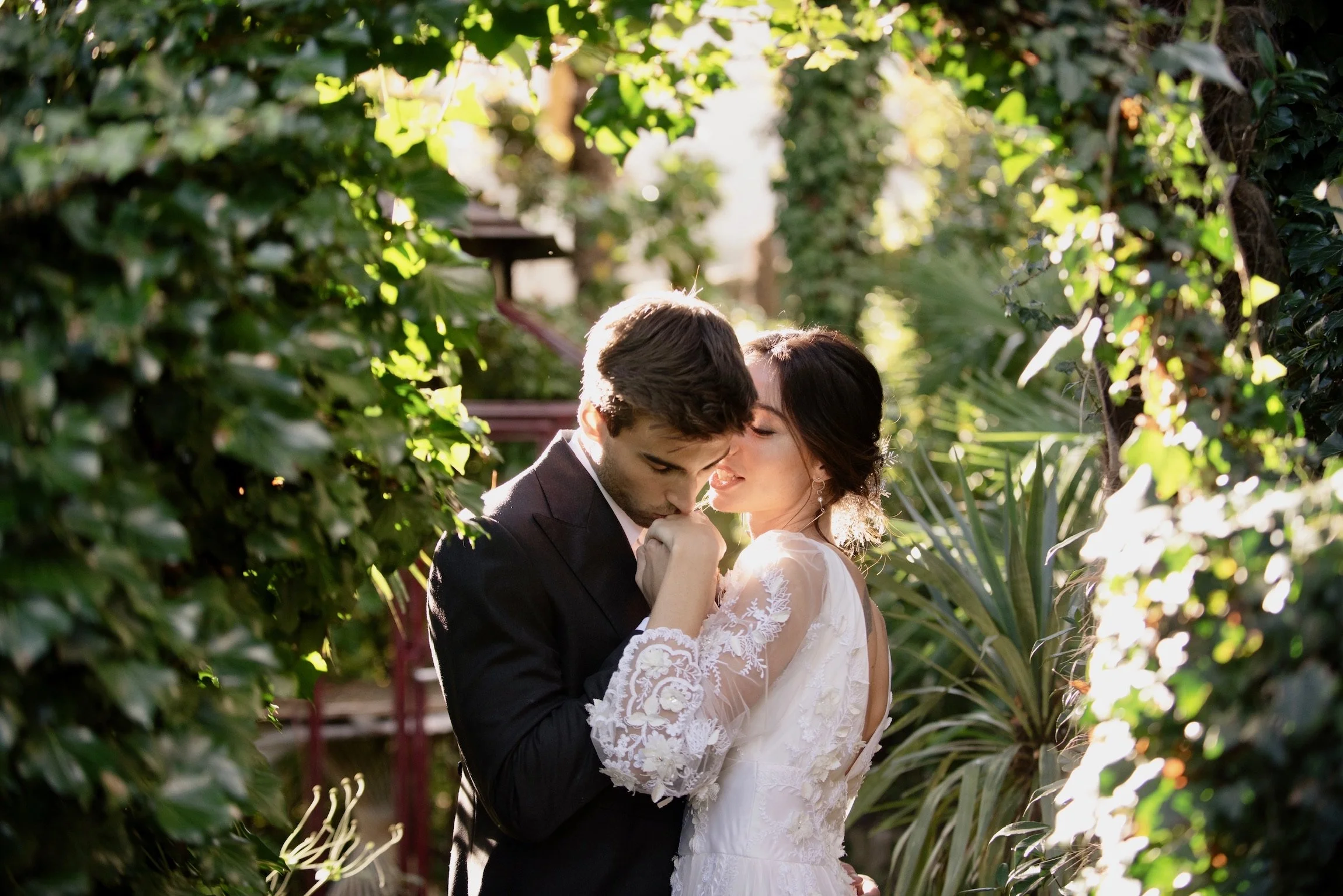 Coppia di sposi in un giardino, con il uomo vestito di nero e la donna in abito bianco, che si baciano in un momento romantico. Microwedding in Como Lake,  Shooting in Como Lake, Engagement in Como Lake, Events in Como Lake. A place for wedding, acco