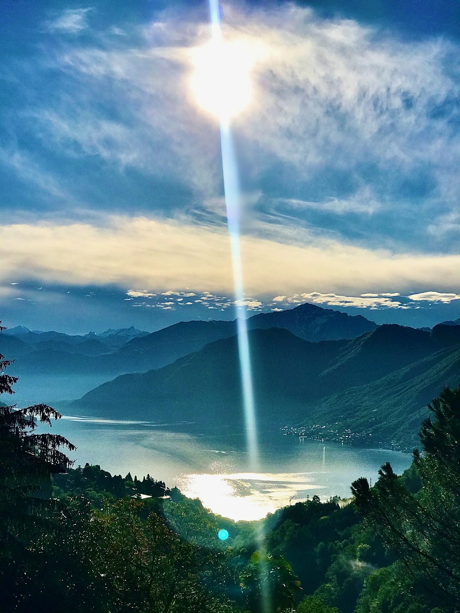 Paesaggio montano con lago e cielo con nuvole, il sole splende con un raggio di luce che attraversa il cielo e riflette sull'acqua. Microwedding in Como Lake,  Shooting in Como Lake, Engagement in Como Lake, Events in Como Lake. A place for wedding,