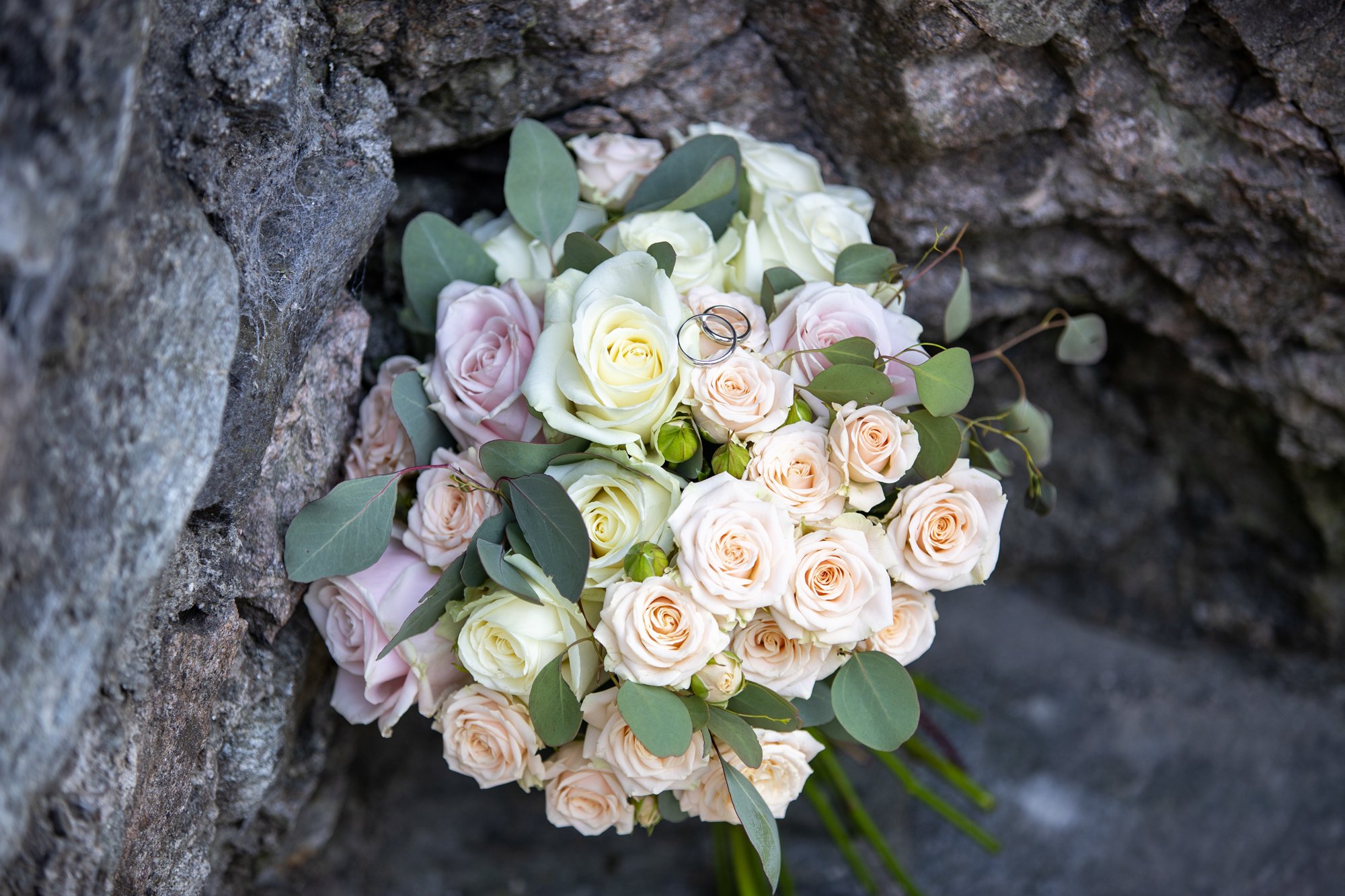 Bouquet di rose bianche, crema e rosa pallido, con foglie di eucalipto, adagiate tra le rocce.