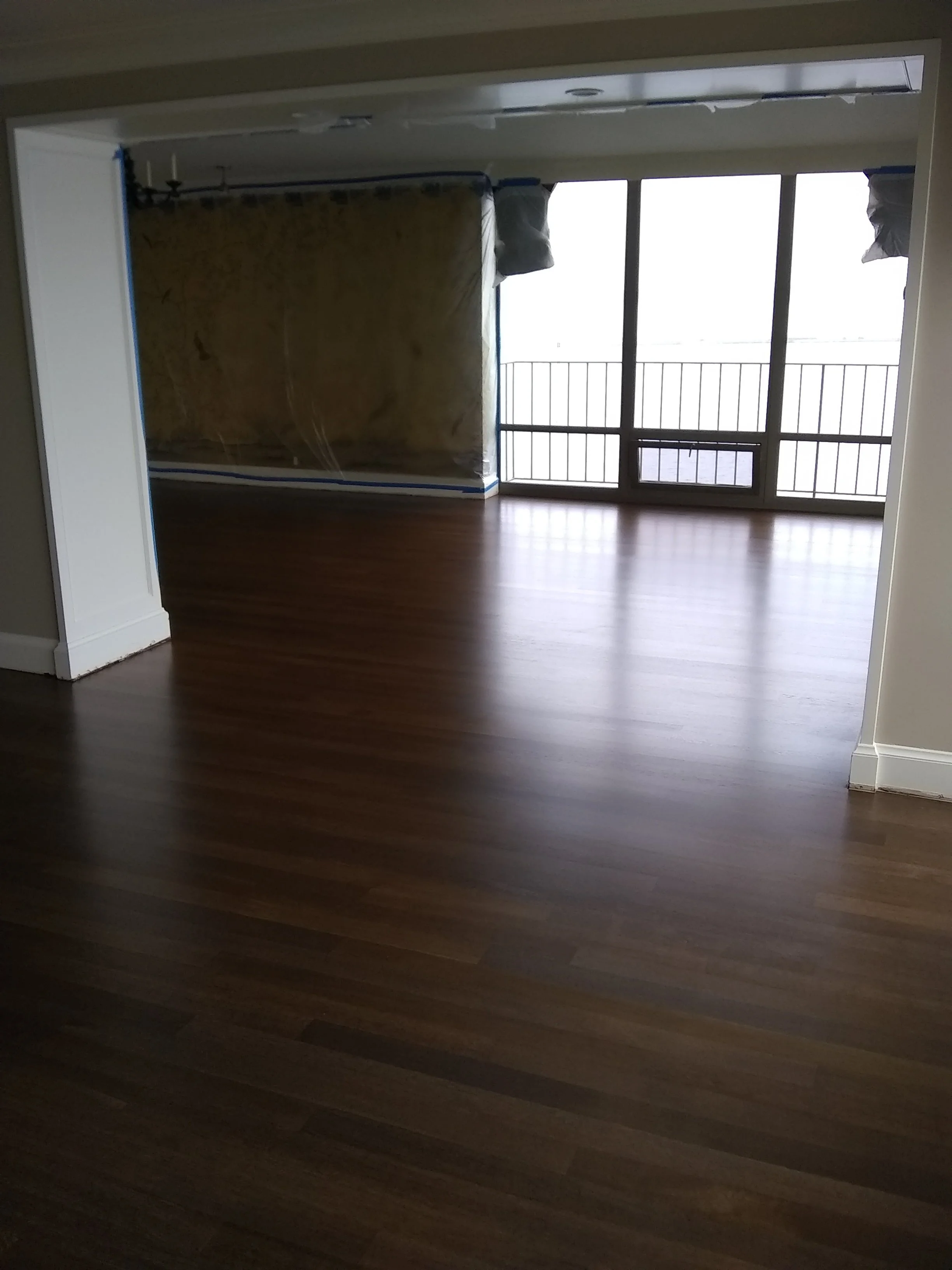 Empty living room with hardwood floors, large window and balcony, partially covered with plastic