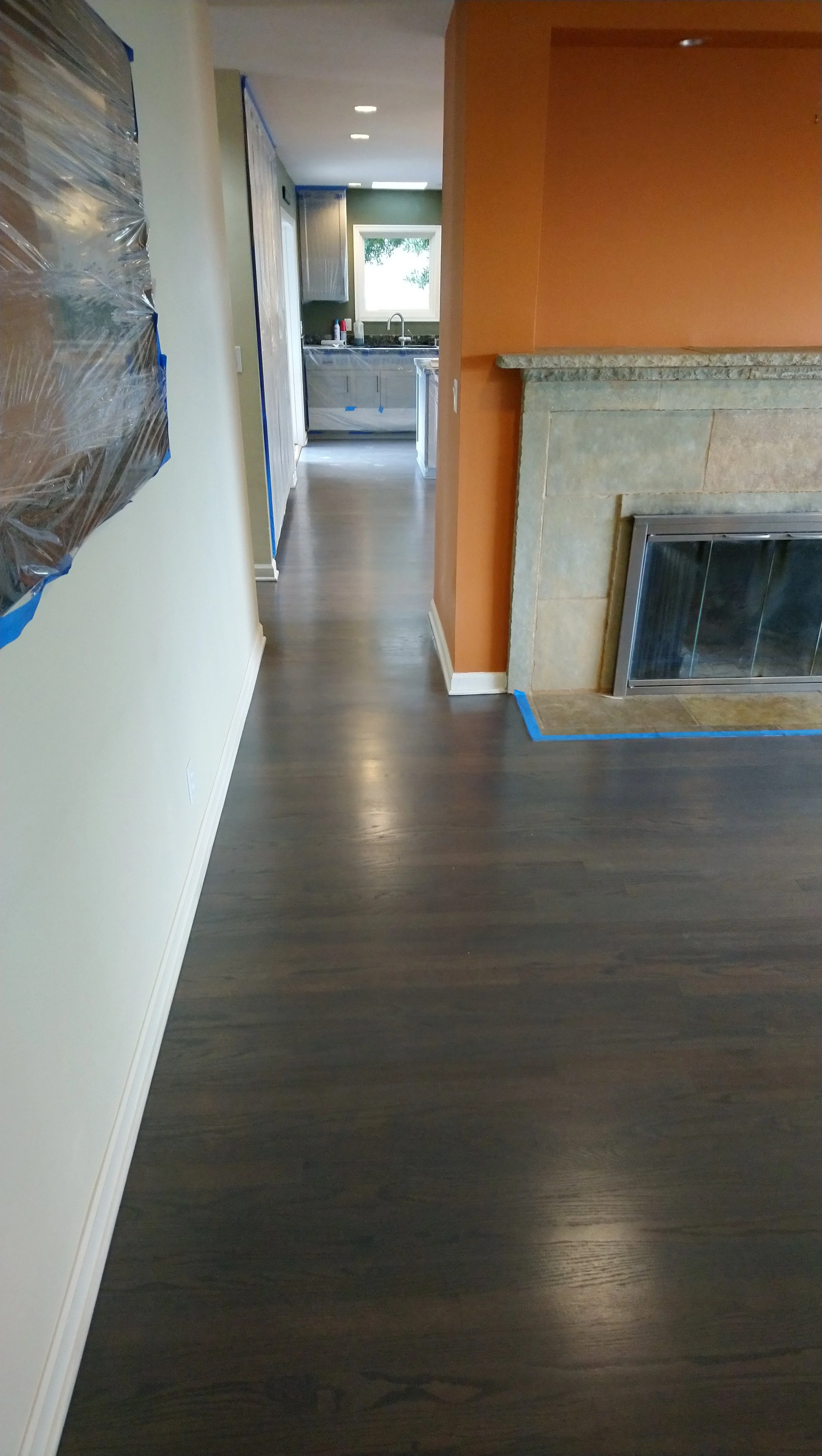 Interior view of a hallway leading to a kitchen, with a fireplace on the right and a wall on the left partially covered with plastic.