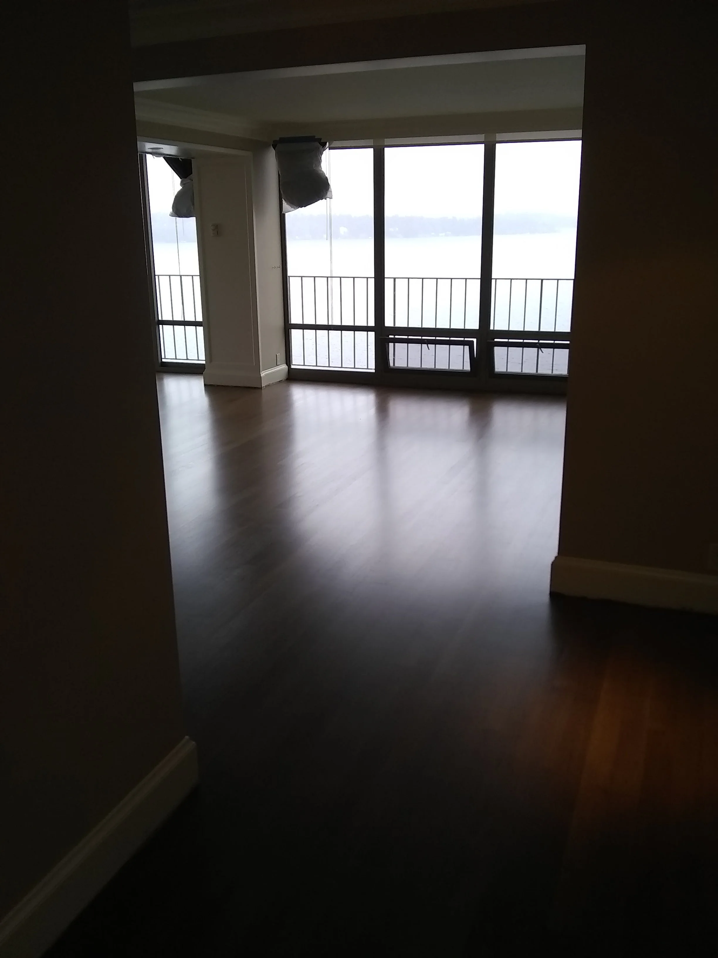 Room with large glass sliding doors offering a view of water and coastline, with some hanging plastic bags or coverings.