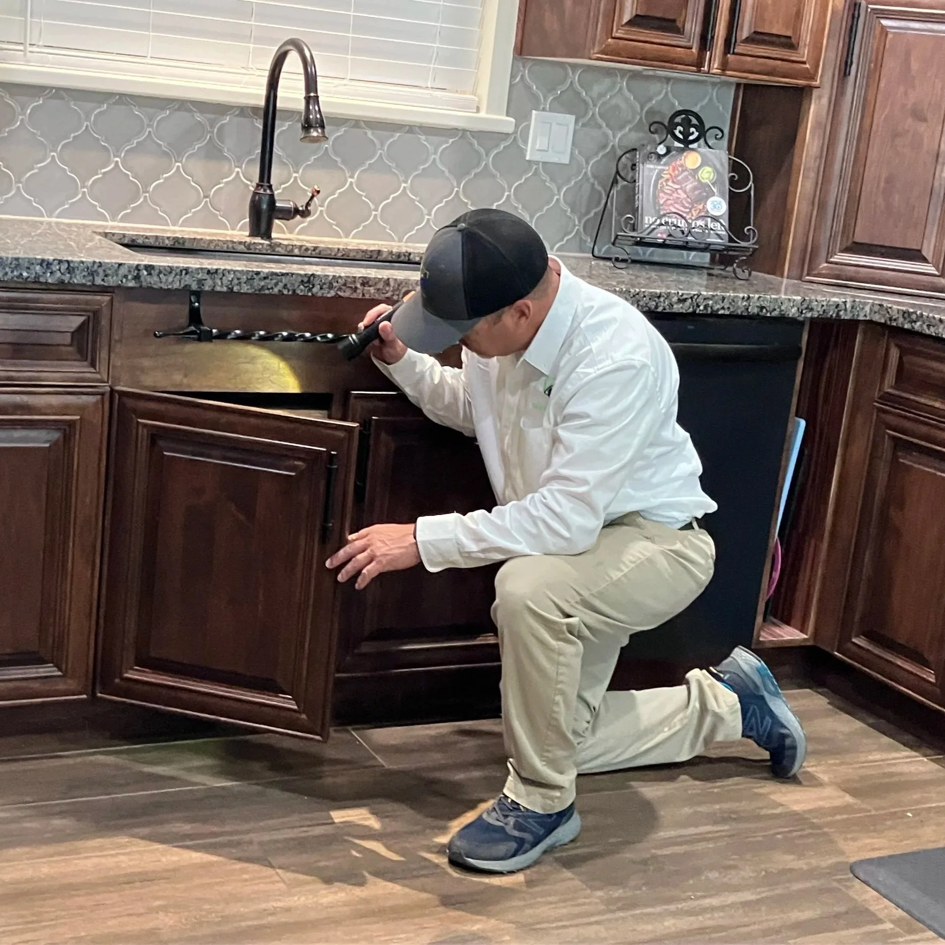Matt, owner of Pest Free AZ, inspecting underneath a kitchen sink for pest entry points and moisture conditions in an East Valley home.